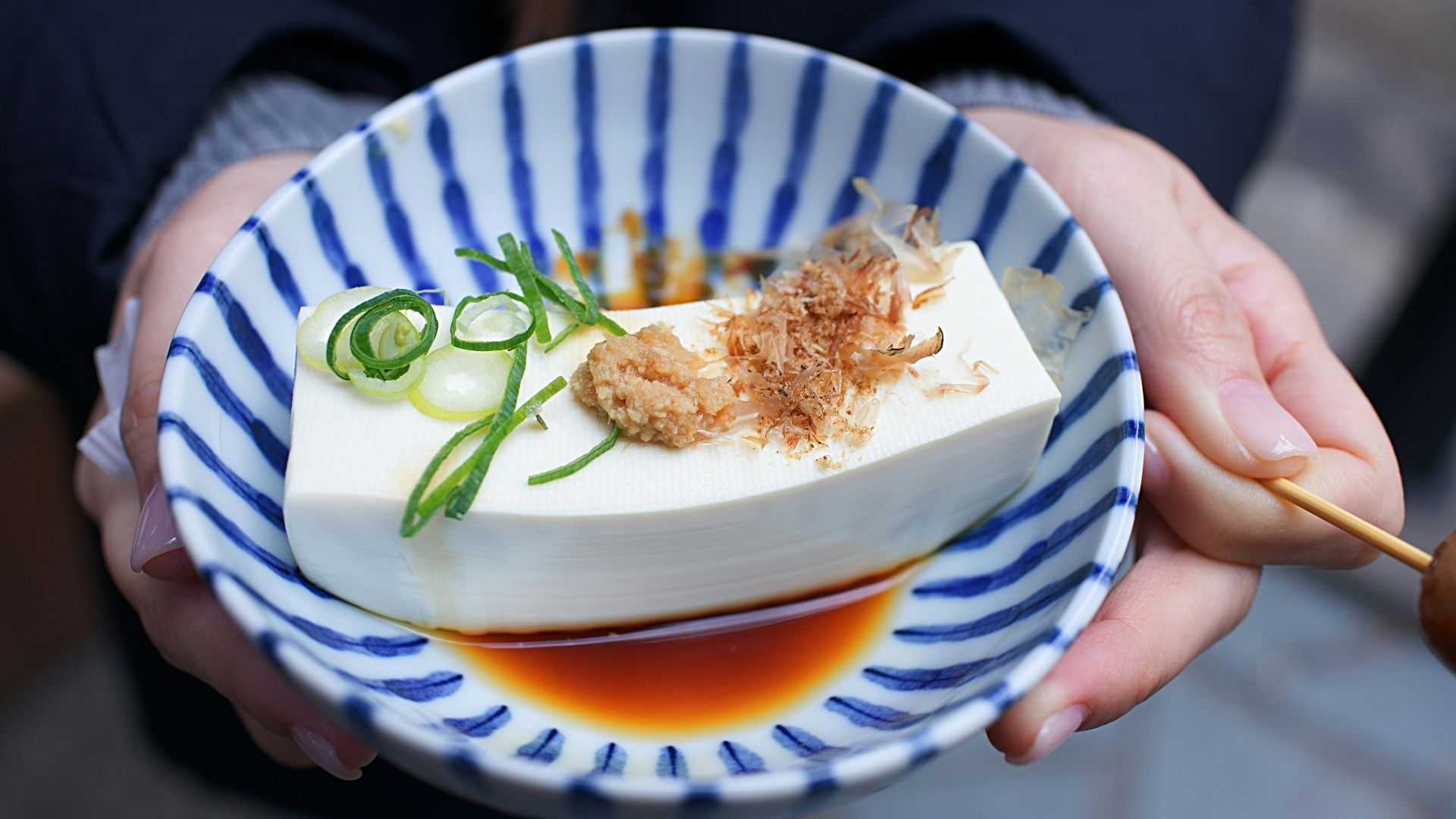 person holding white and blue ceramic plate with rice and sliced cucumber