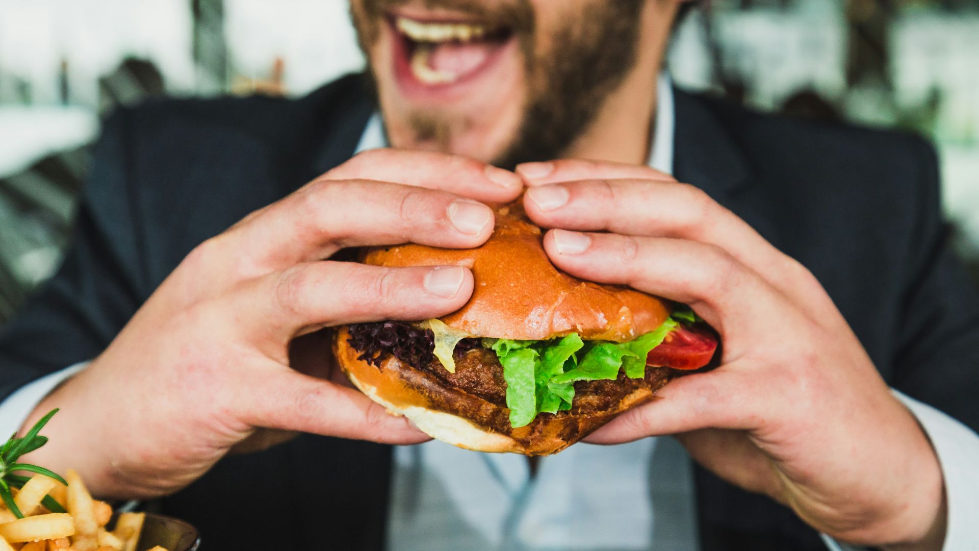 person holding burger bun with vegetables and meat