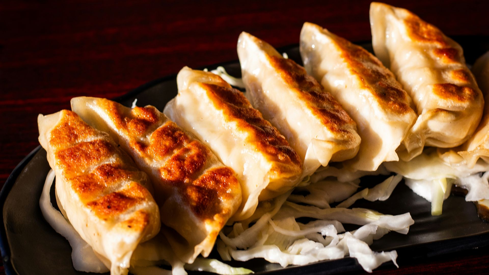 A black plate topped with dumplings on top of a wooden table