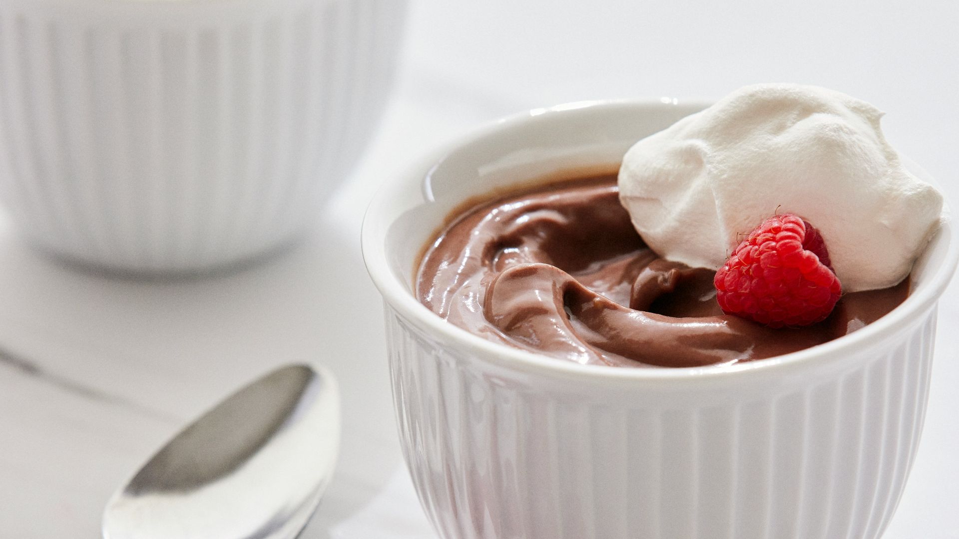 two bowls of chocolate pudding with raspberries on the side