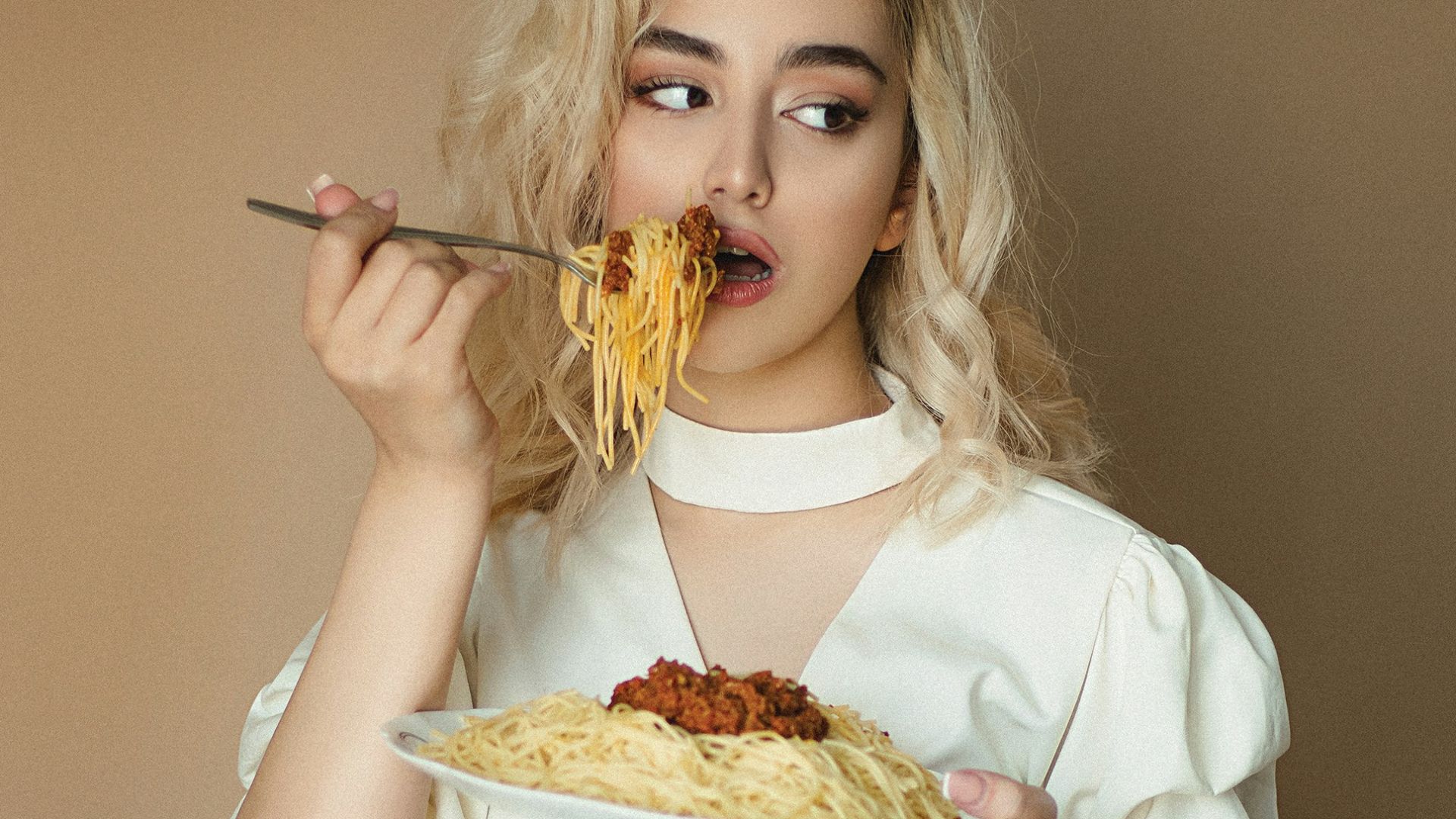 woman in white long sleeve shirt holding fork and eating pizza
