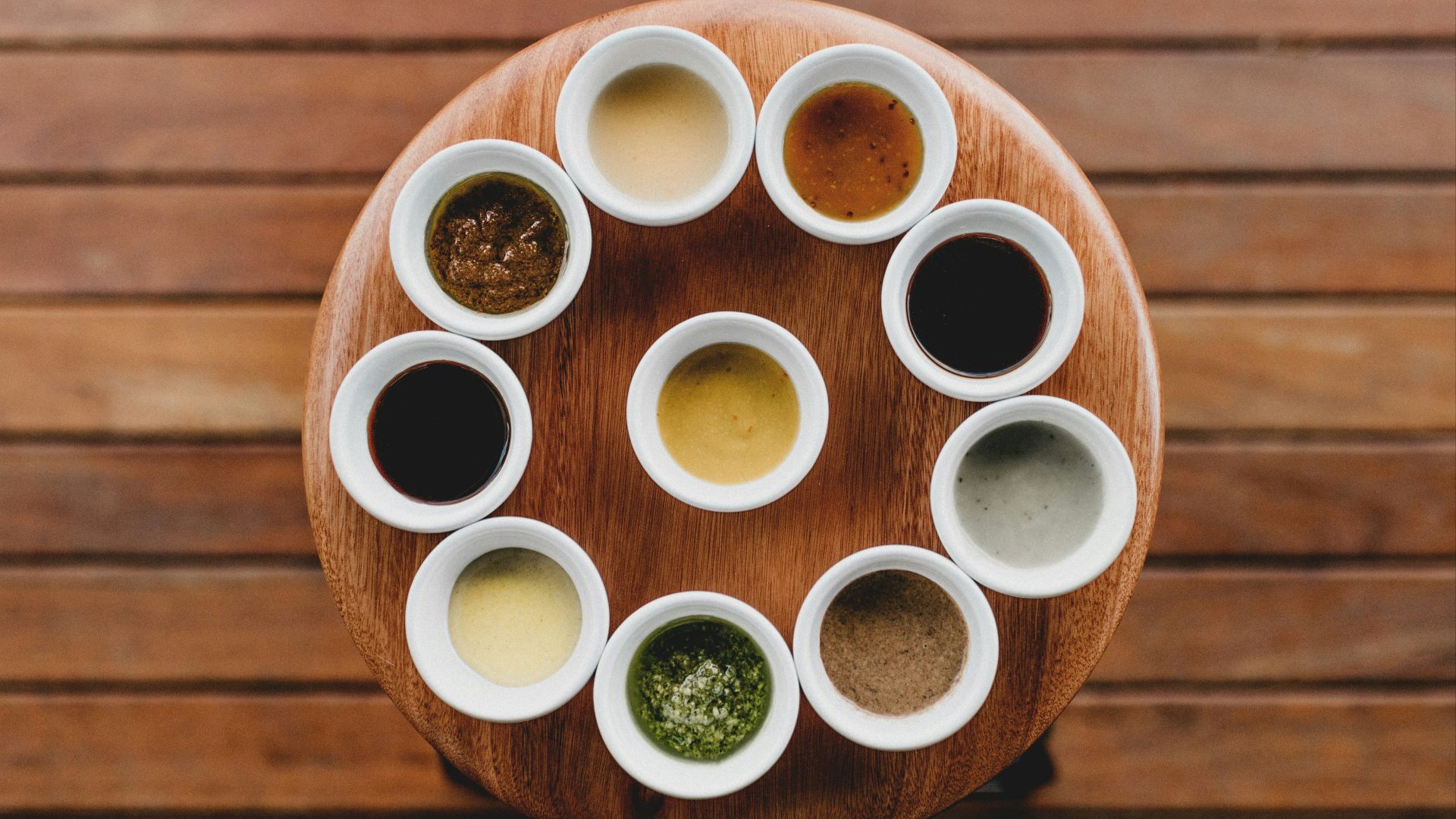 a wooden table topped with white cups filled with sauces