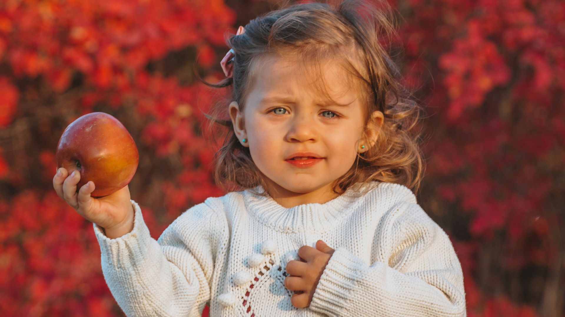 girl in white sweater holding brown round fruit