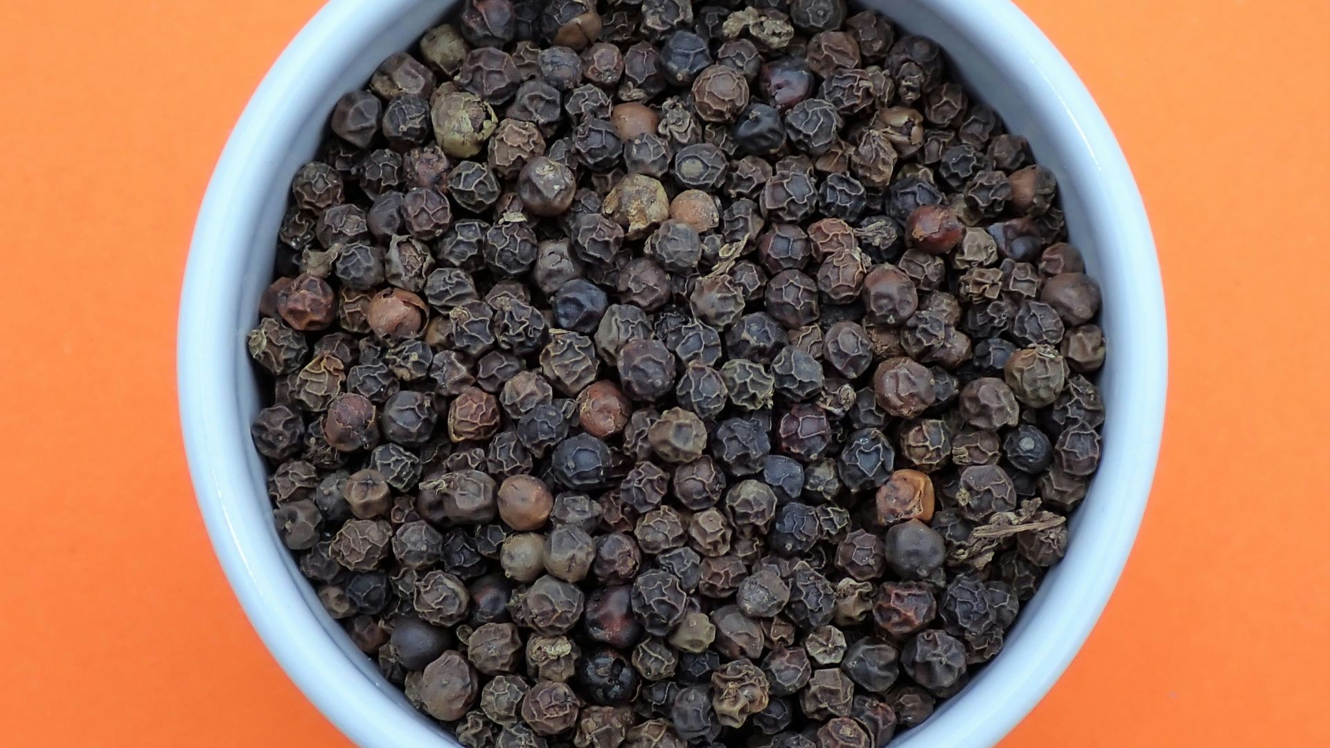 a bowl of black pepper on an orange background
