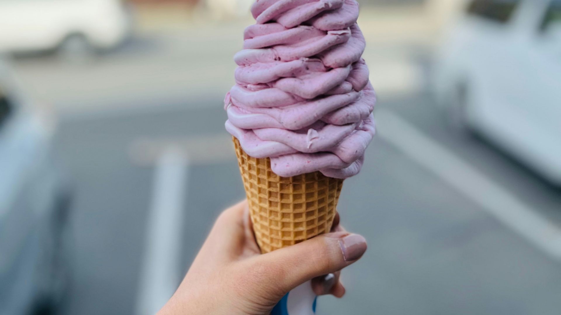 A person holding a pink ice cream cone in a parking lot
