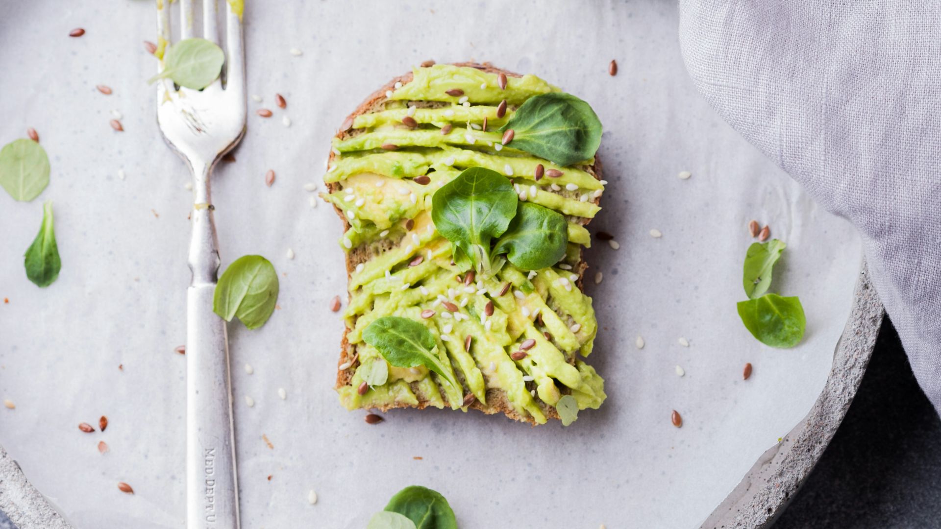 wheat bread with avocado spread beside white plastic spoon and pressed lime on round white plate