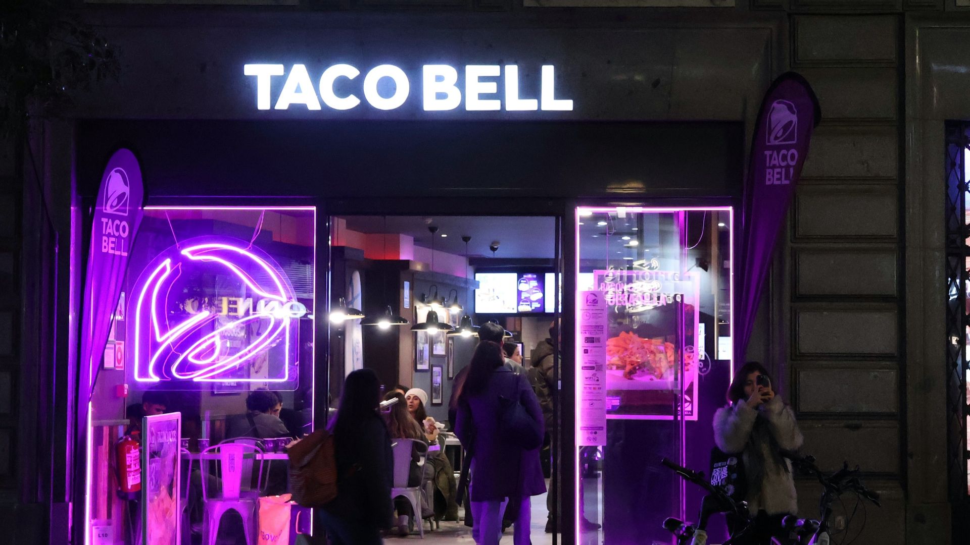 A purple lit store front with people walking by