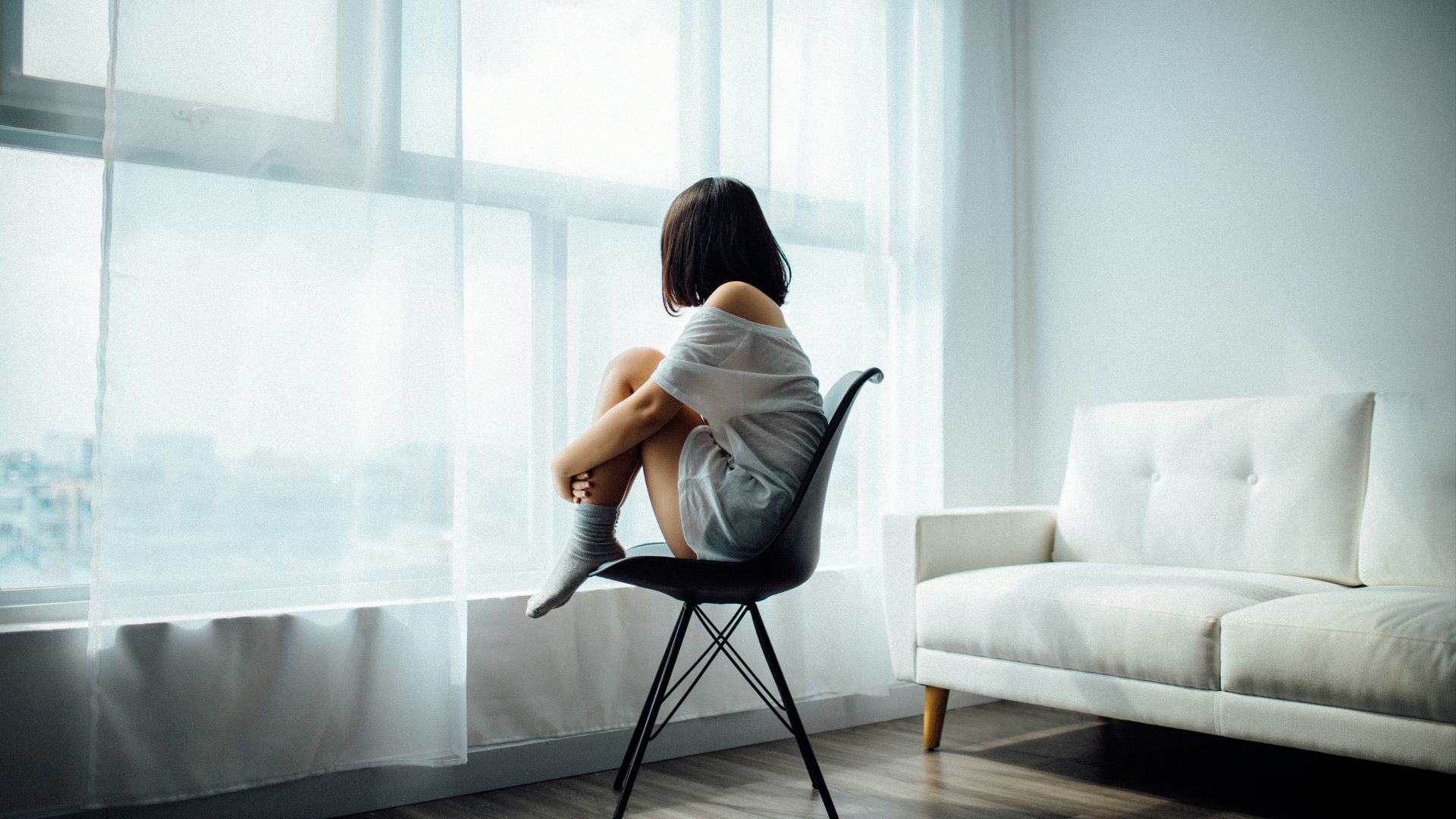 woman sitting on black chair in front of glass-panel window with white curtains