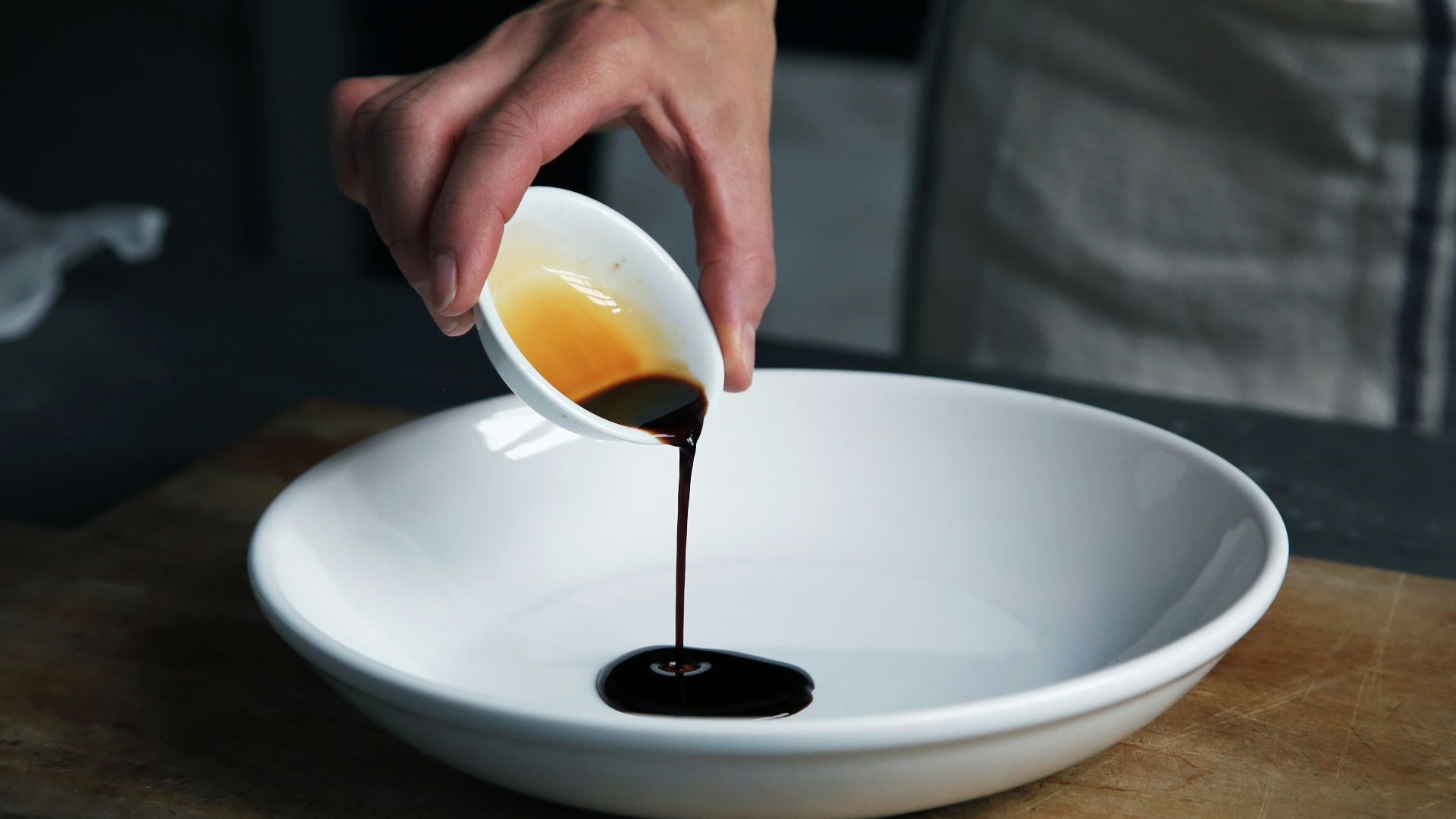 person dripping black liquid from small white ceramic bowl to big white ceramic bowl