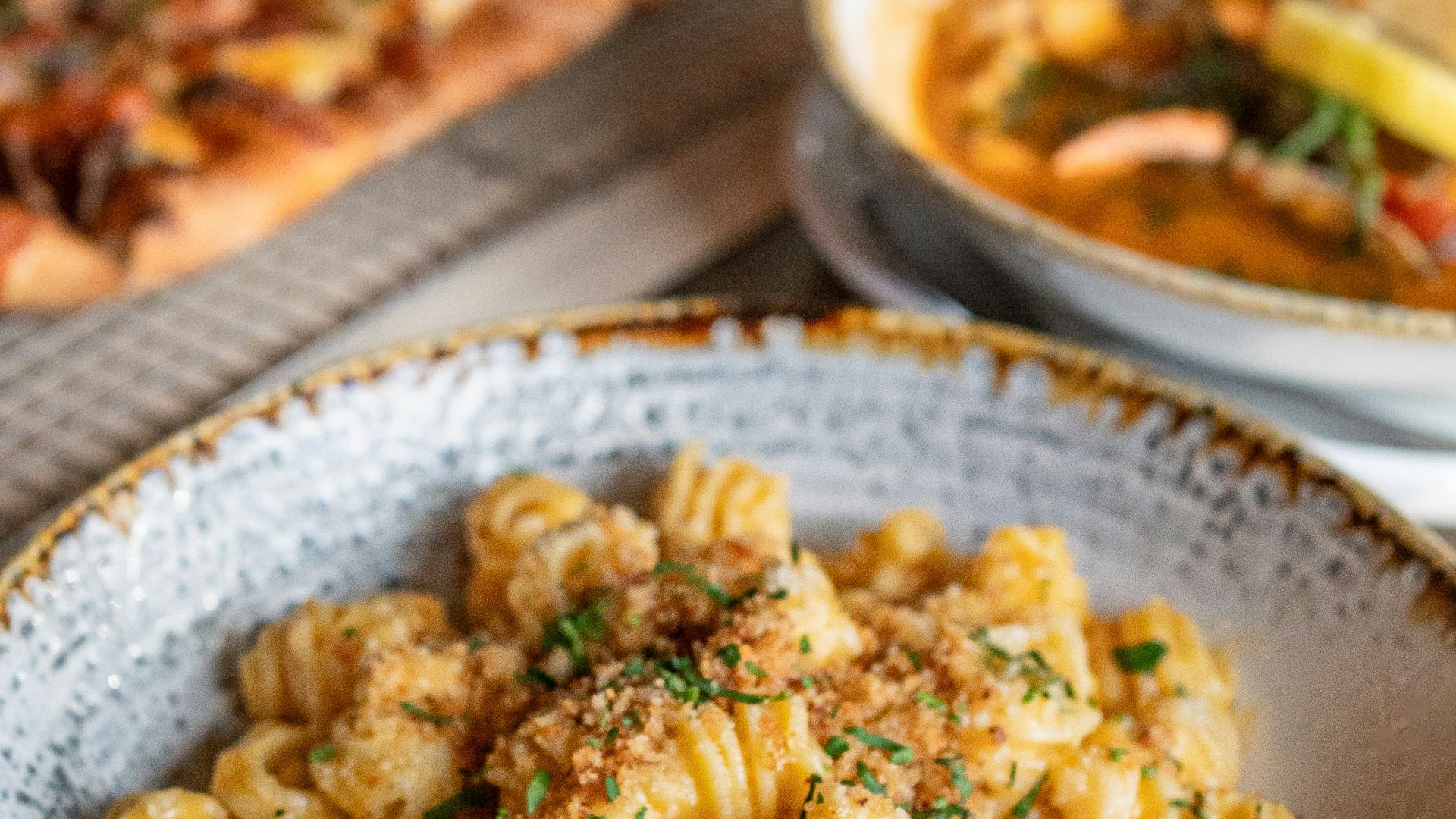 a bowl of pasta and a plate of pizza on a table