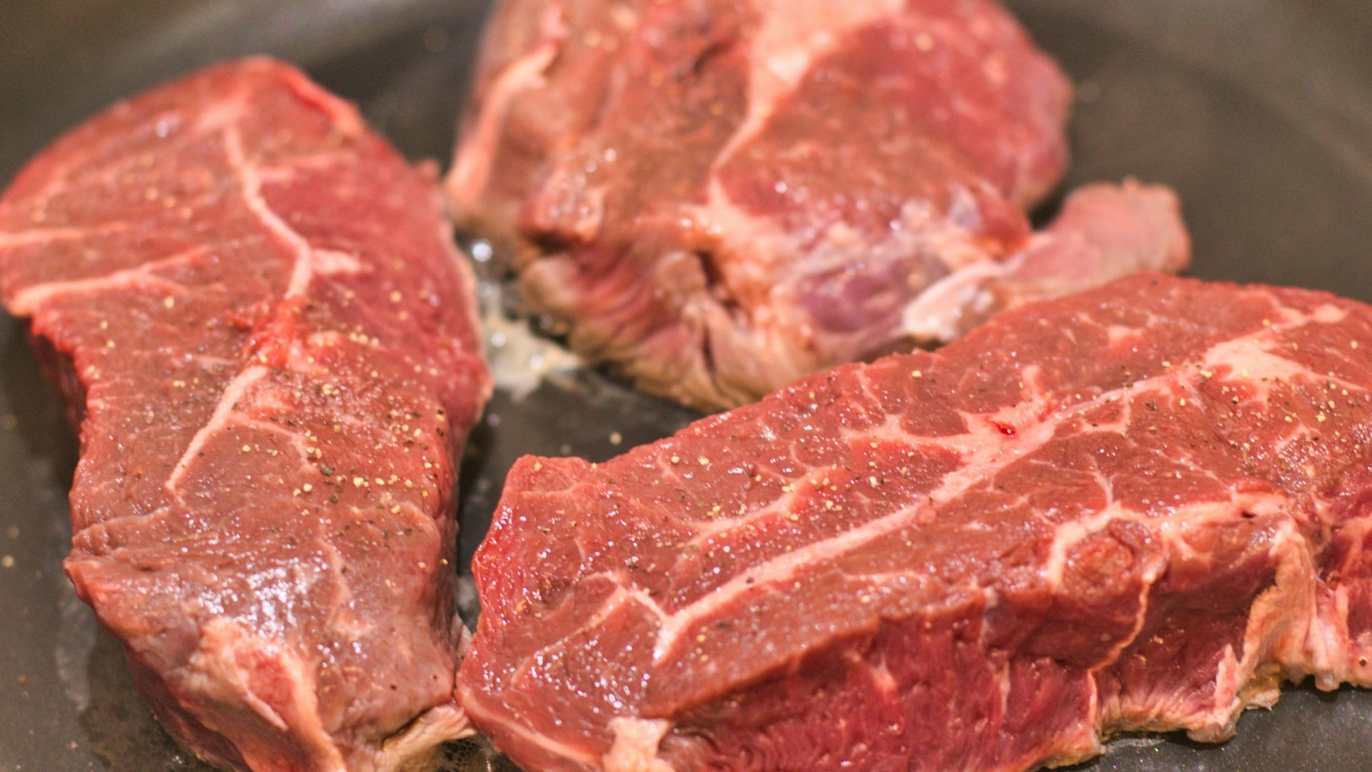 three steaks are cooking in a frying pan