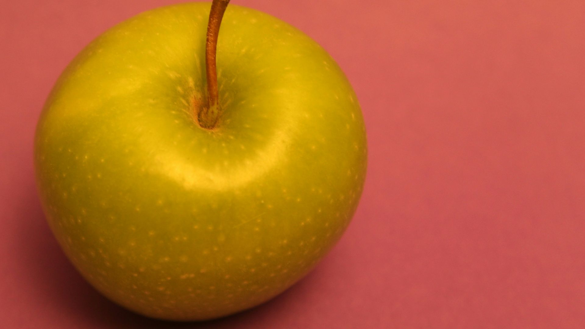 A green apple on a pink background.