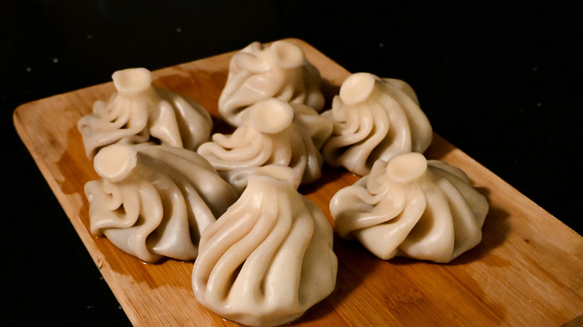 a wooden cutting board topped with dumplings on top of a table