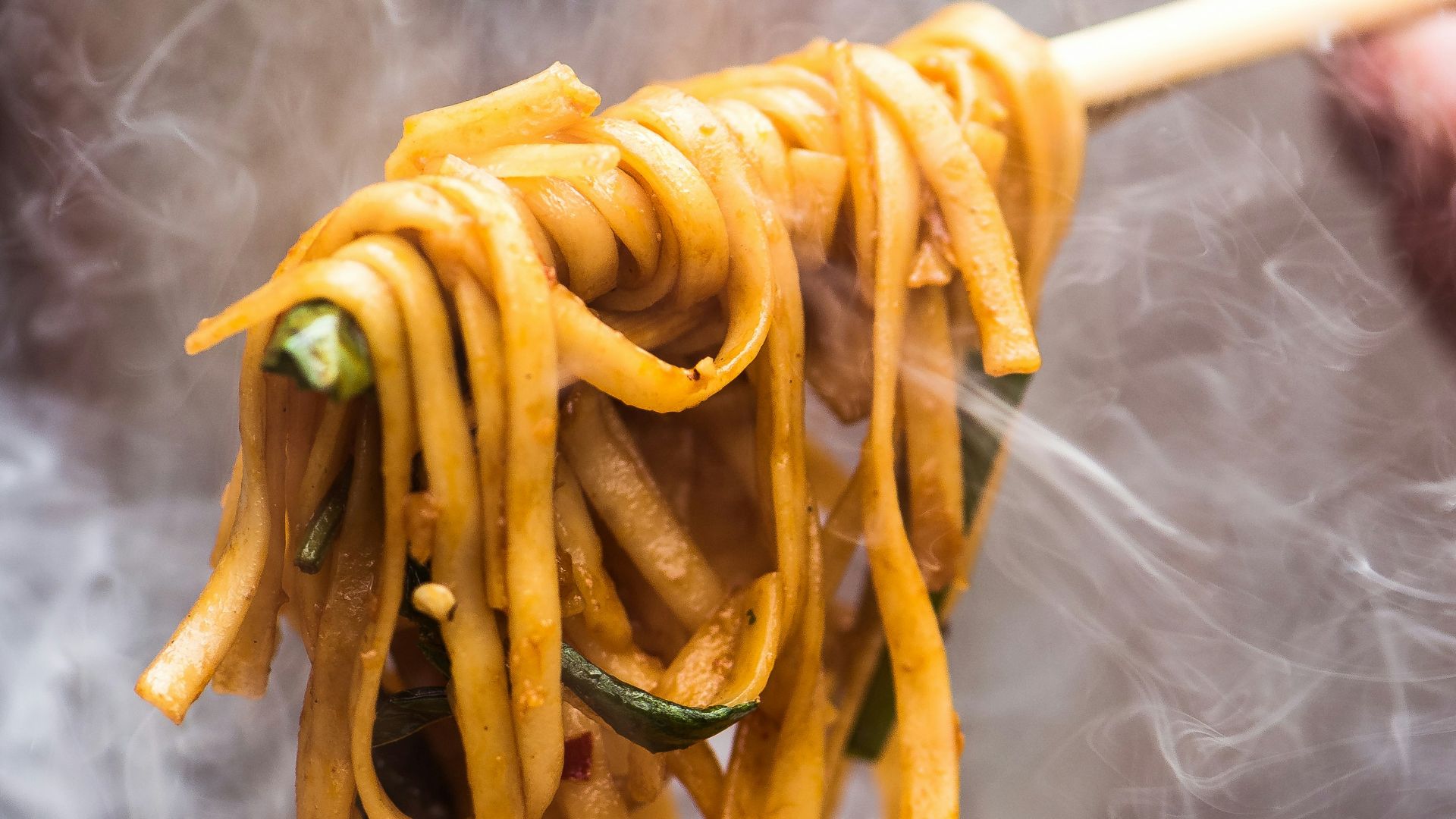 a person holding a wooden spoon full of noodles