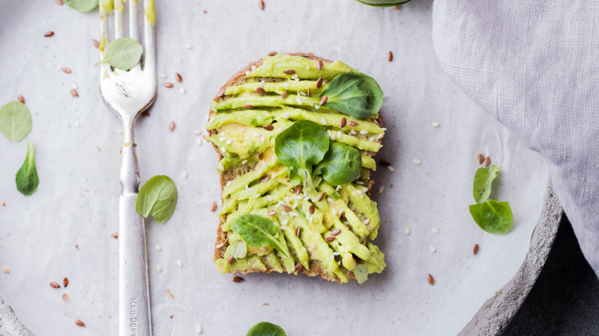 wheat bread with avocado spread beside white plastic spoon and pressed lime on round white plate