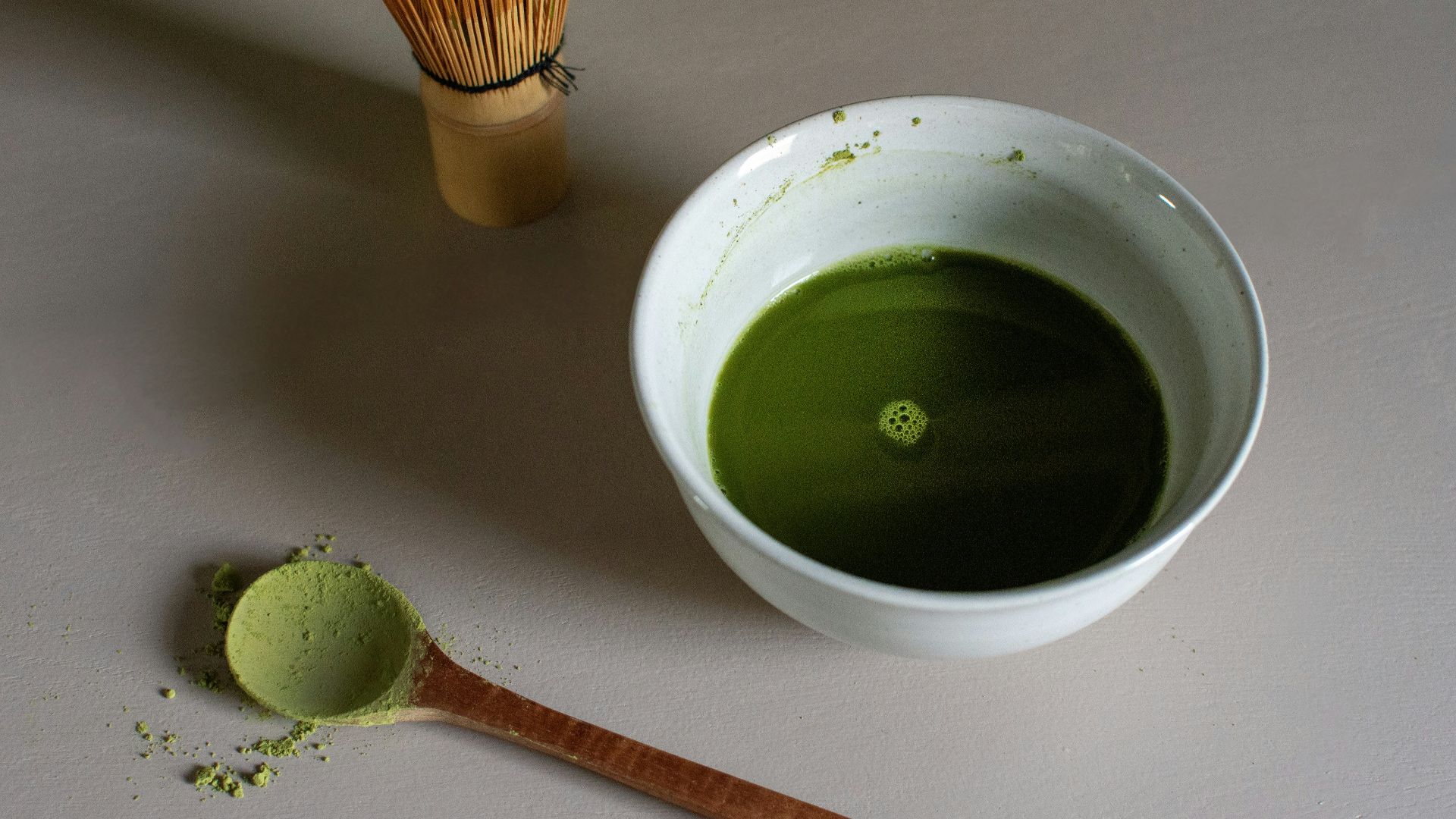 a bowl of green liquid next to a whisk