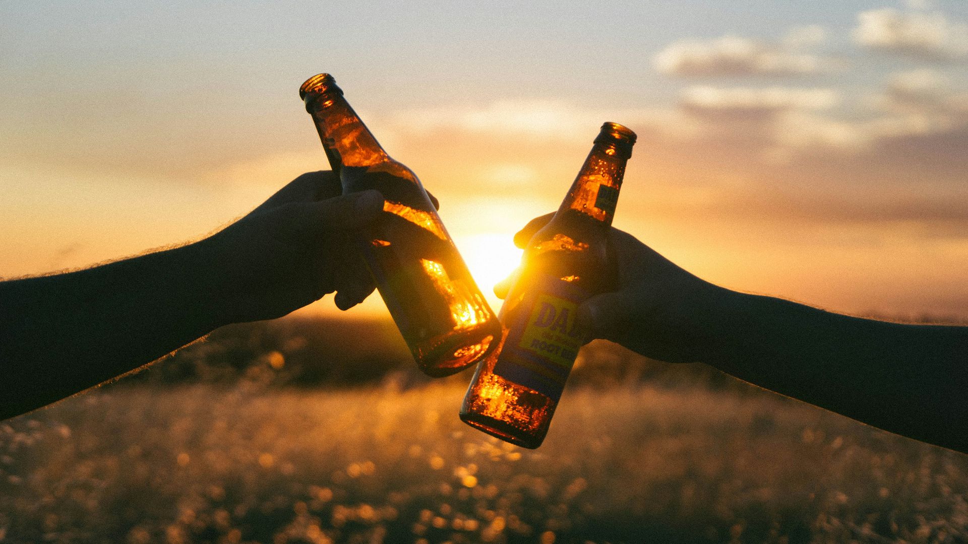photography of person holding glass bottles during sunset