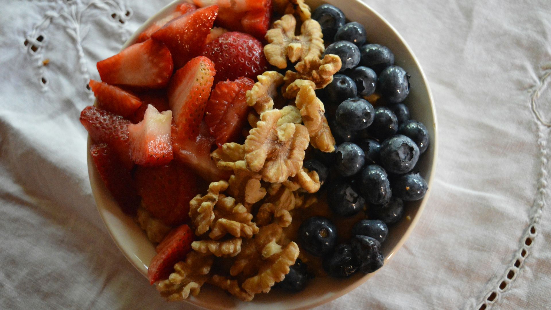 a bowl of cereal, berries, walnuts, and blueberries