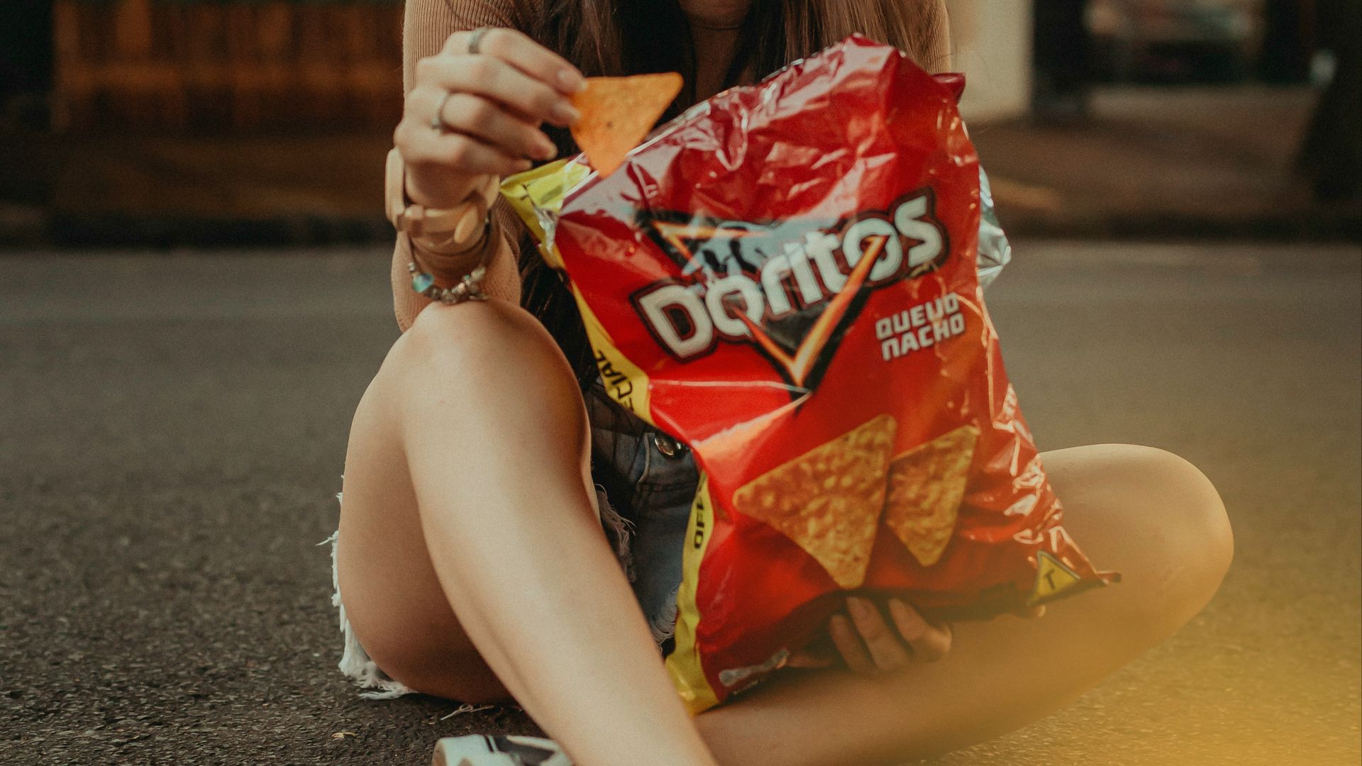 woman in brown shirt sitting on the street holding red and white plastic pack during daytime