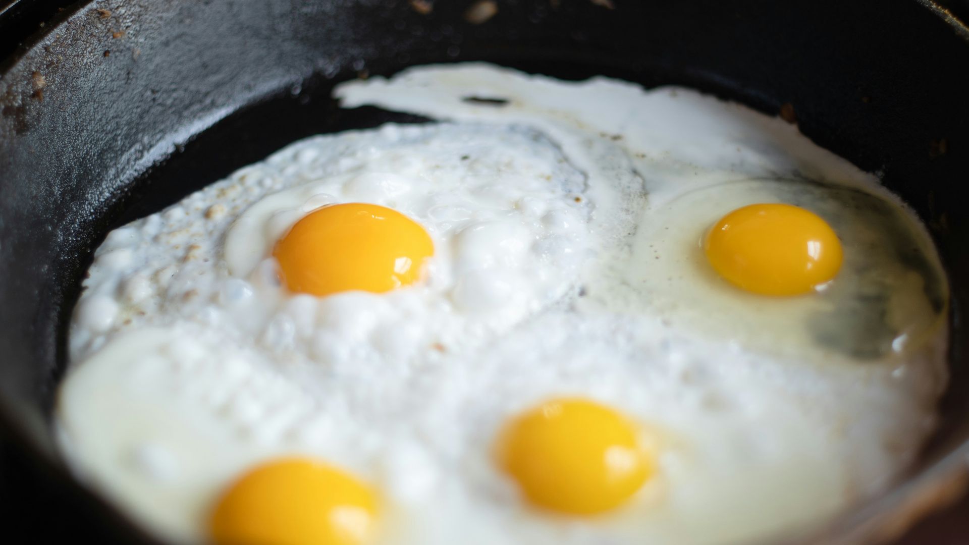three fried eggs in a frying pan on a stove