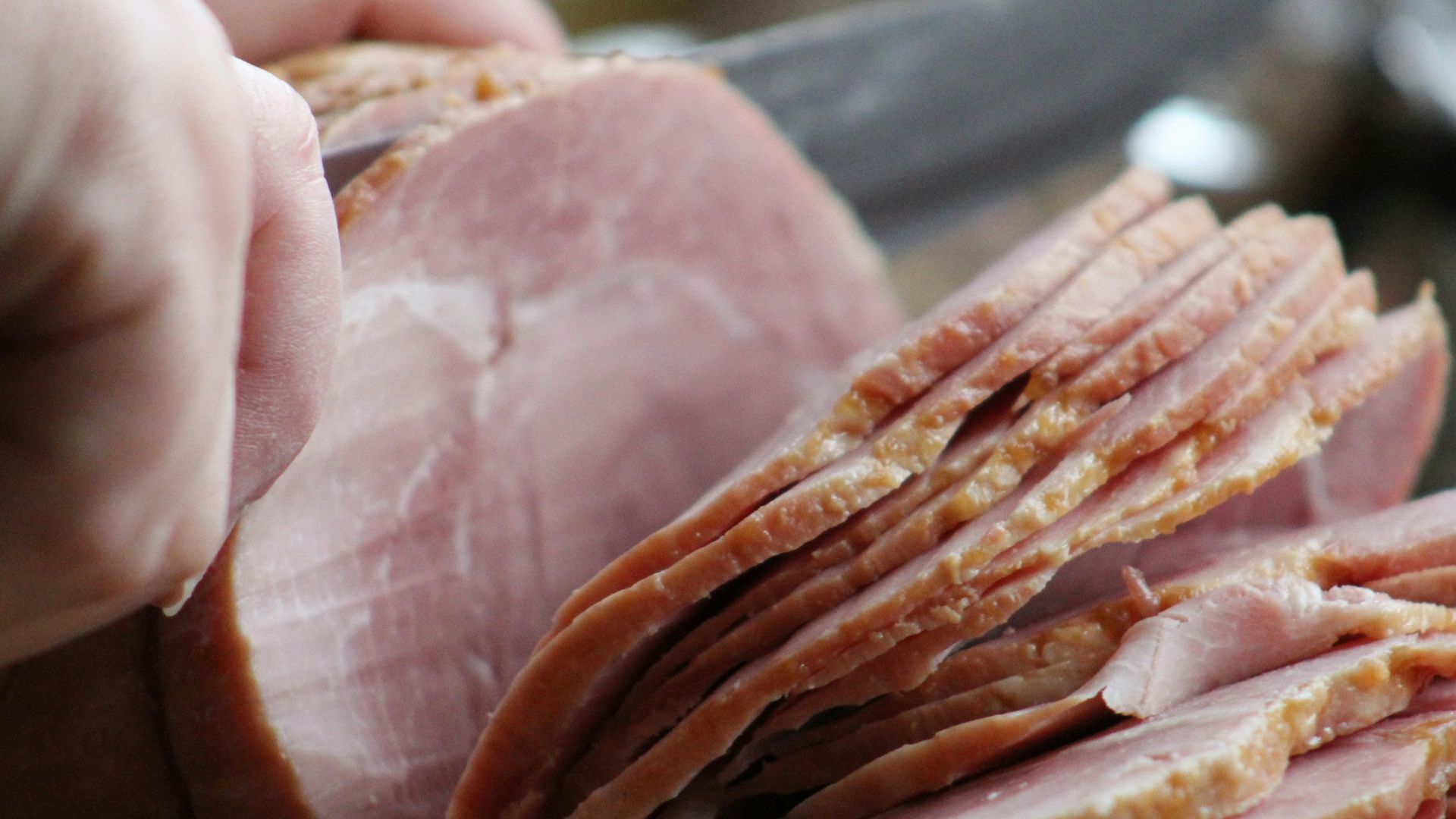 a person slicing ham on a cutting board