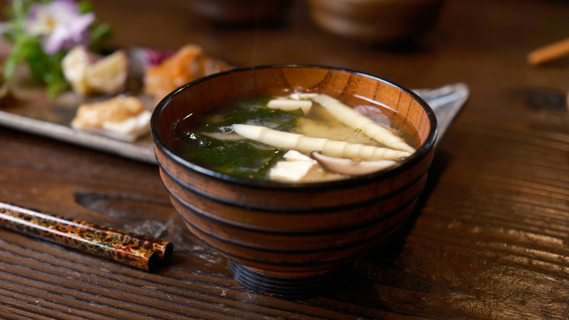 a wooden bowl filled with soup next to chopsticks