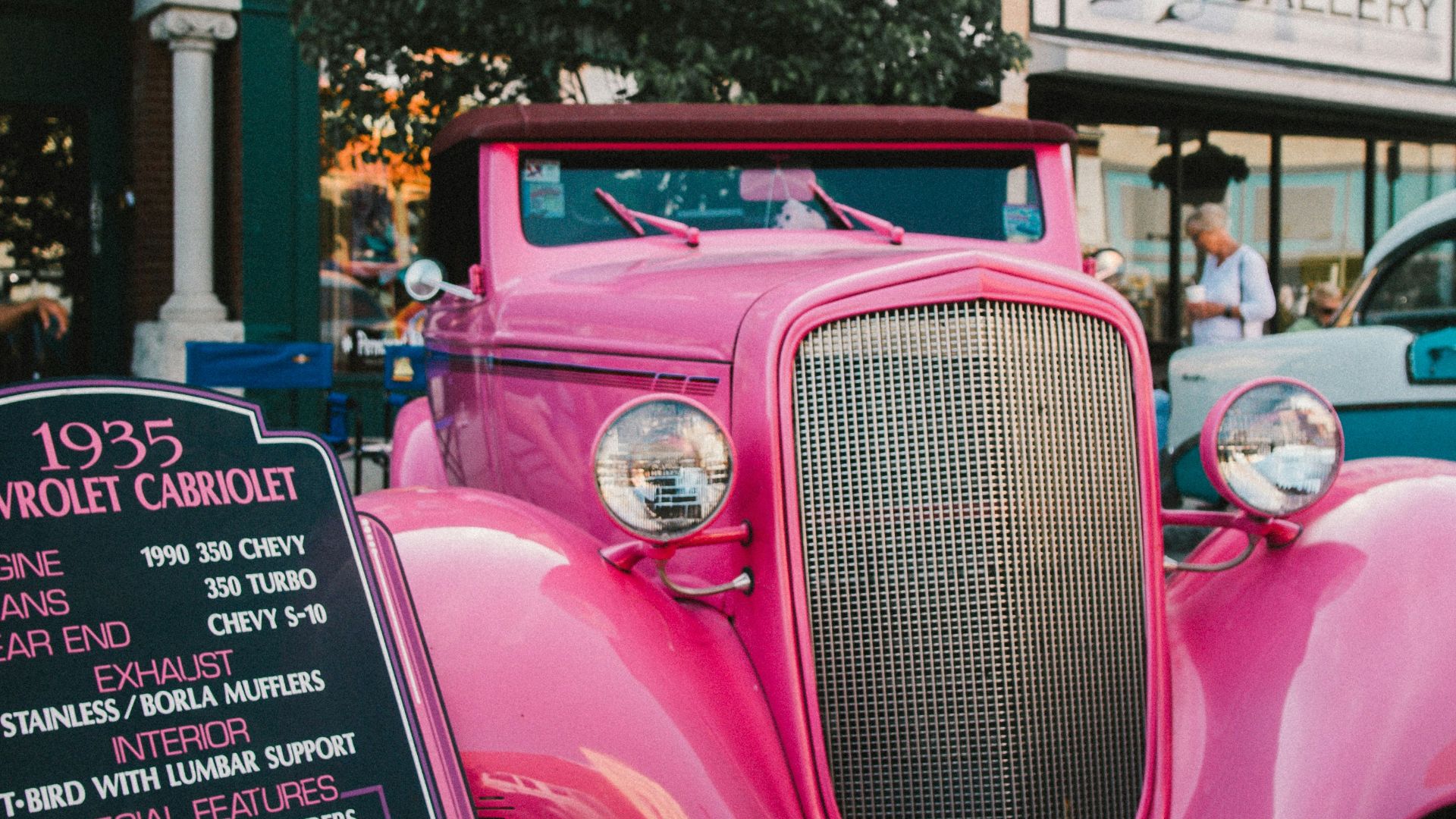 pink vintage car parked near green tree during daytime