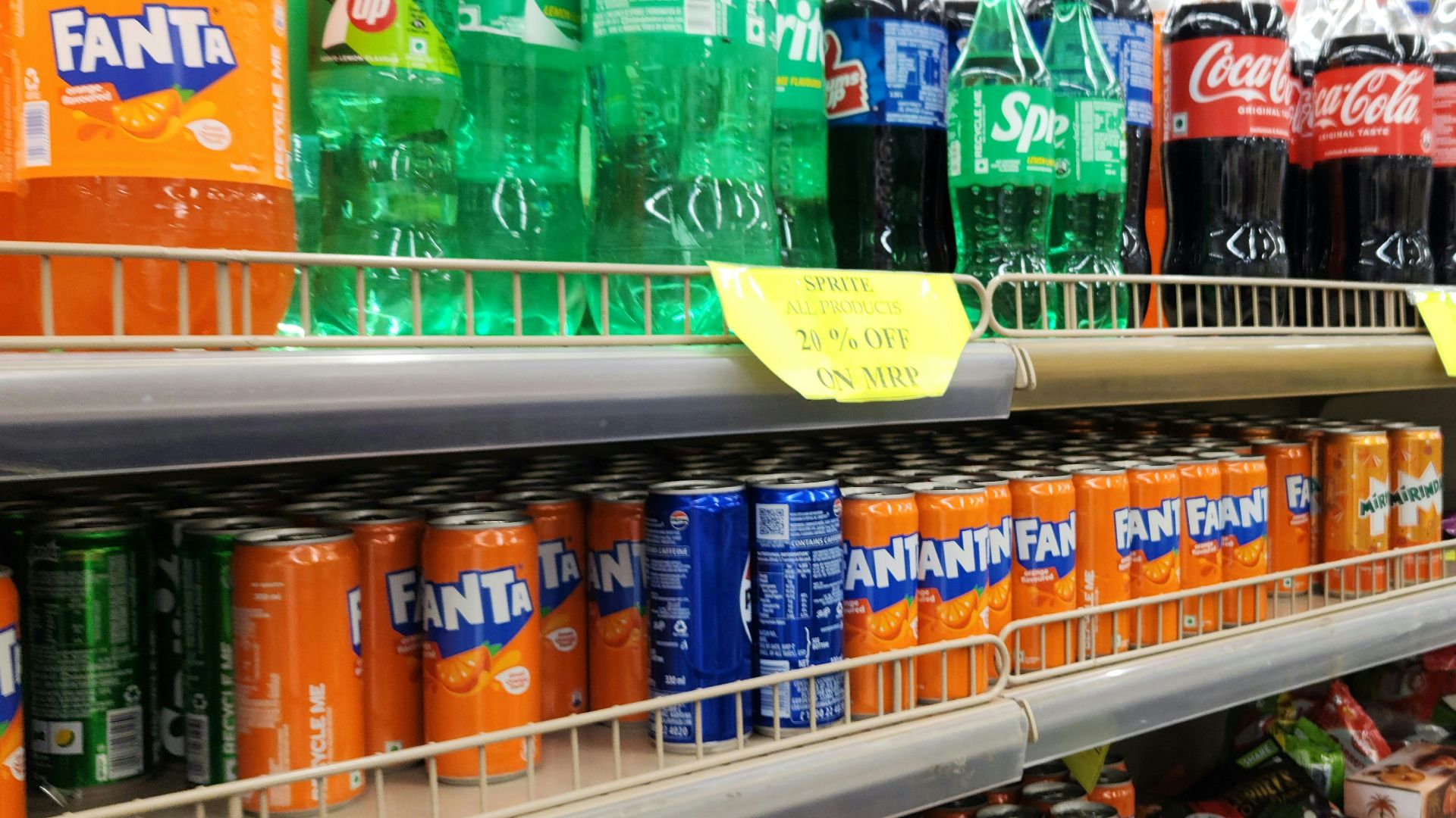 Soda bottles and cans are stocked on supermarket shelves.
