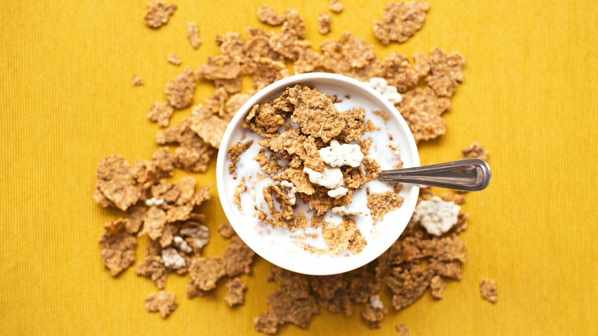 top view of corn flakes in bowl with milk and silver spoon