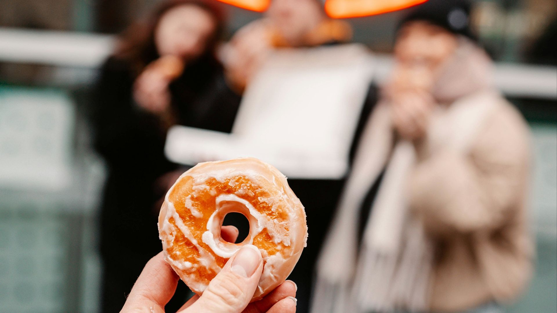 person holding brown donut with orange and white toppings