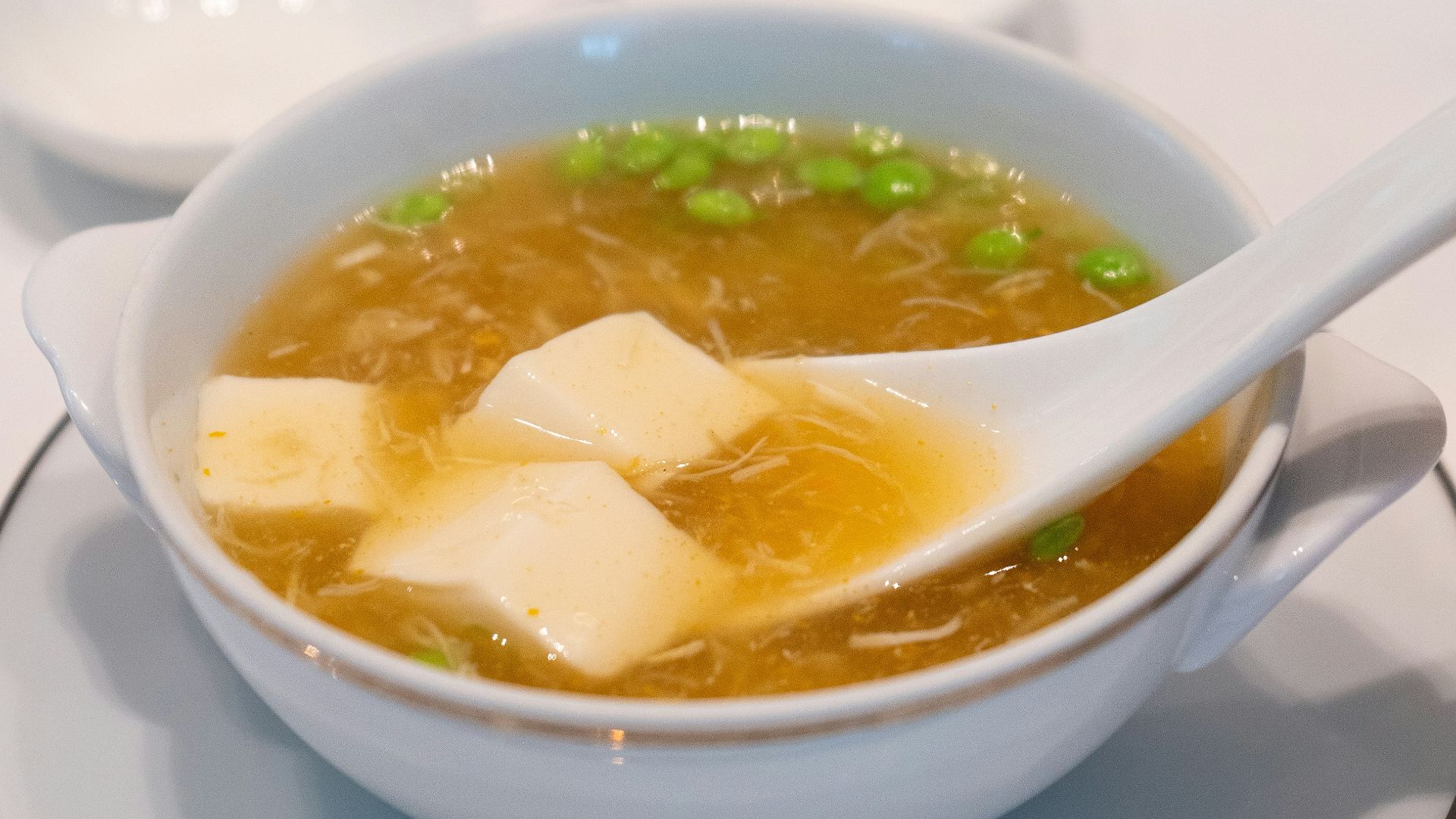 A bowl of soup on a plate with two spoons