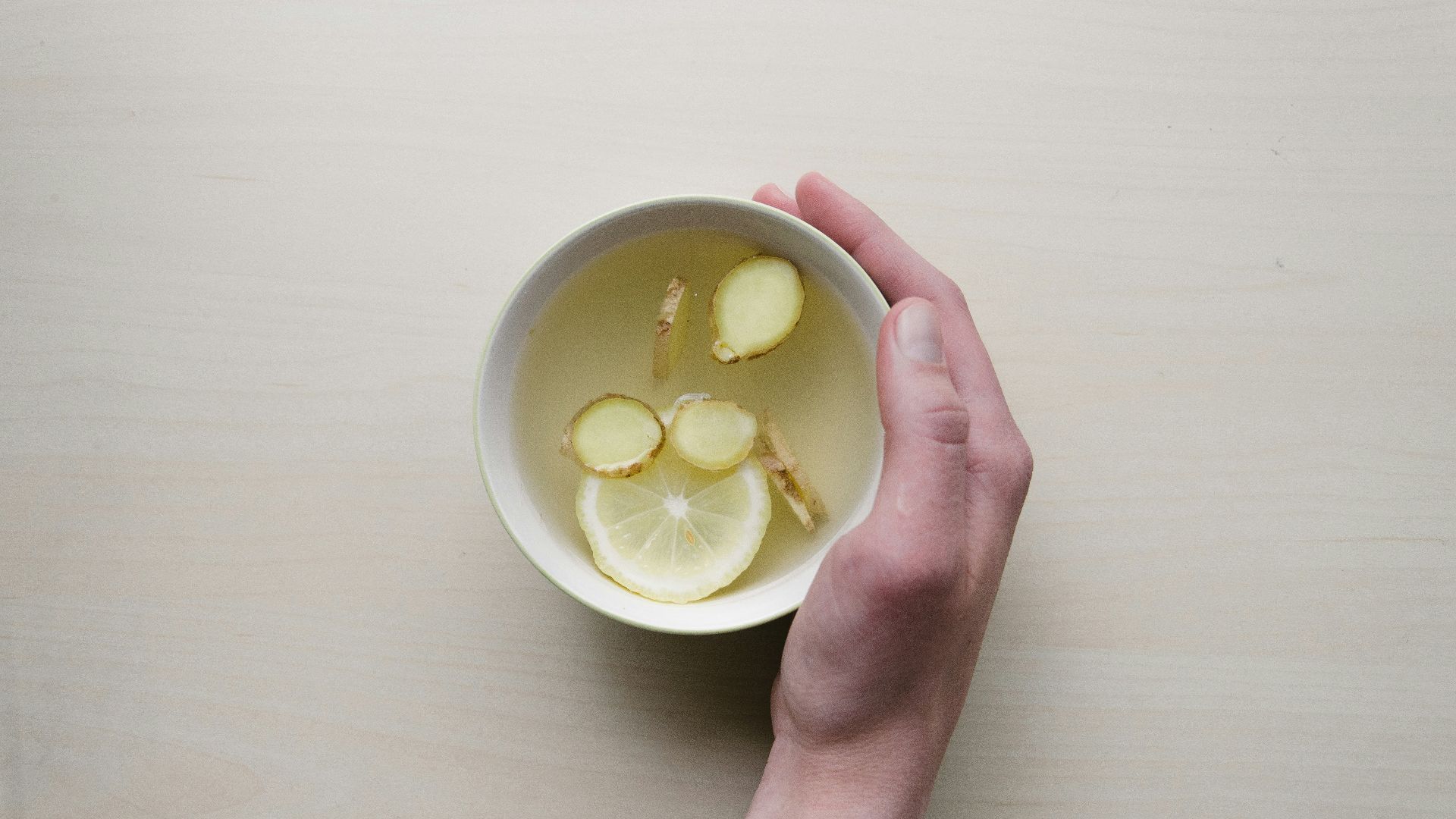 person holding white bowl with sliced lime and ginger inside