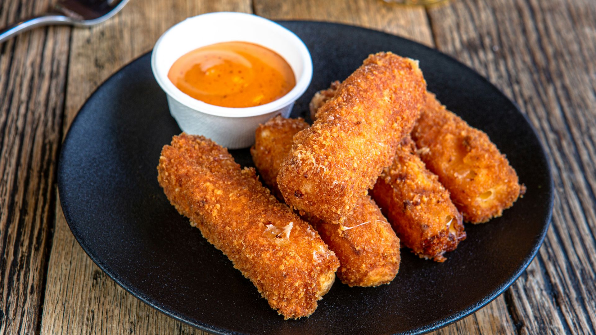 A black plate topped with fried food next to a cup of dipping sauce