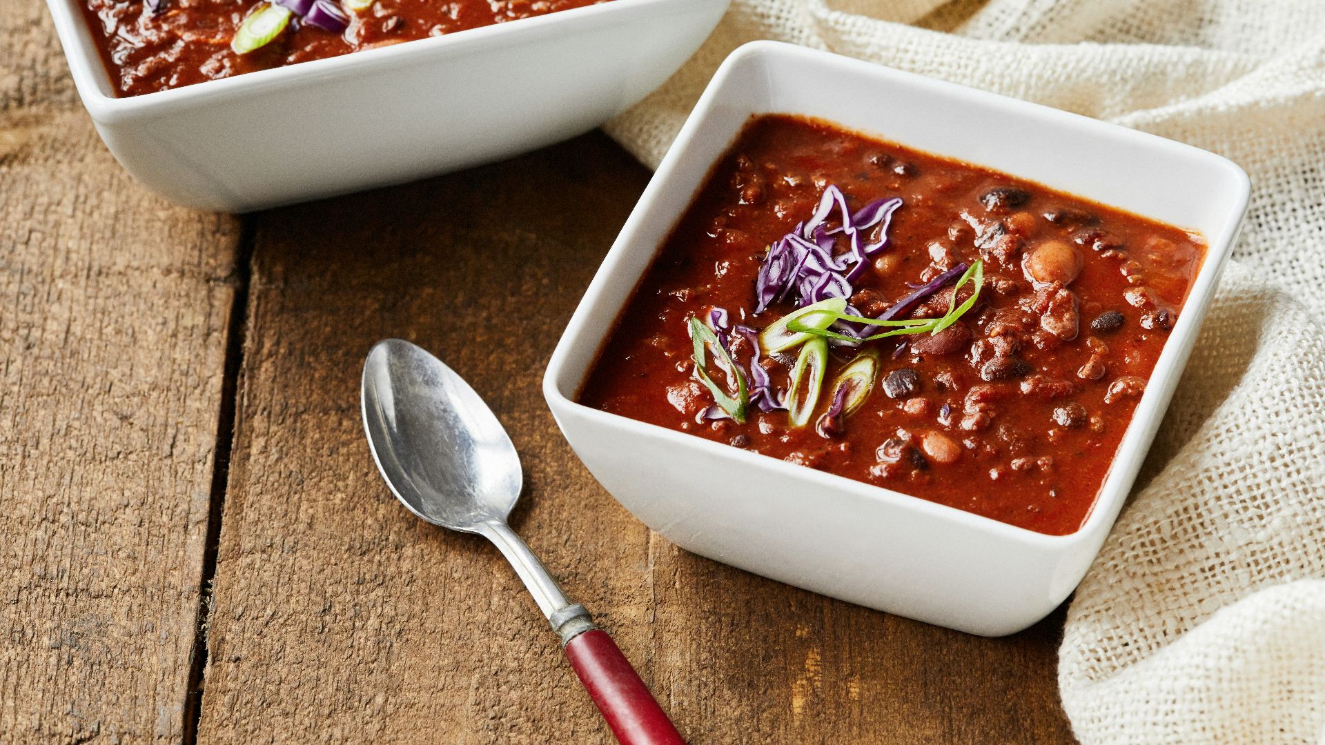 two bowls of chili and a spoon on a wooden table