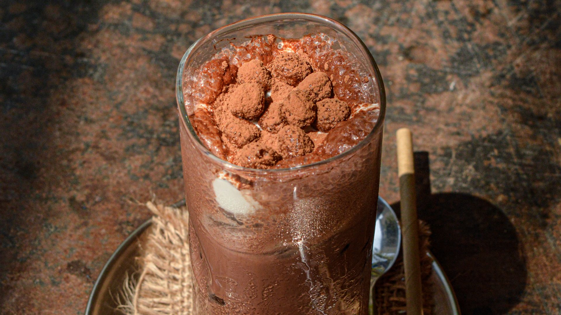 A glass of chocolate pudding on a plate with a spoon