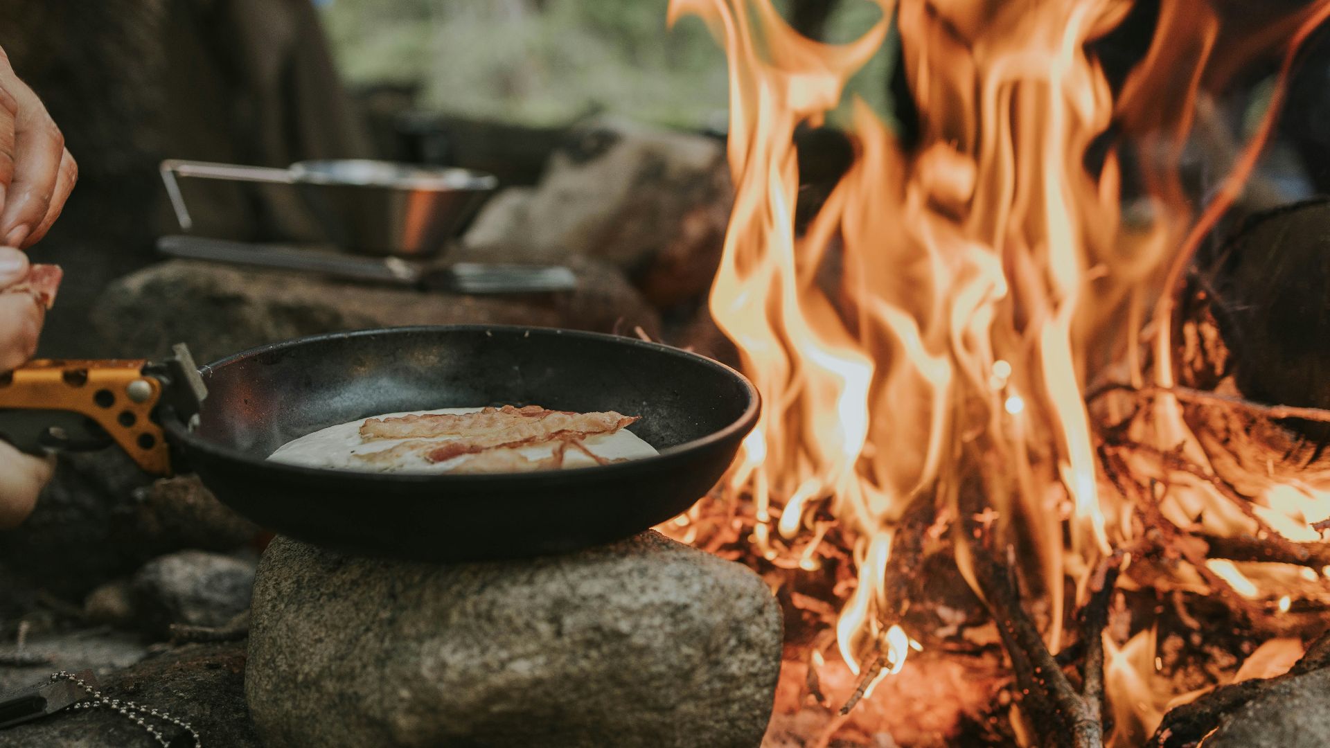 a person cooking food over a skillet over a campfire