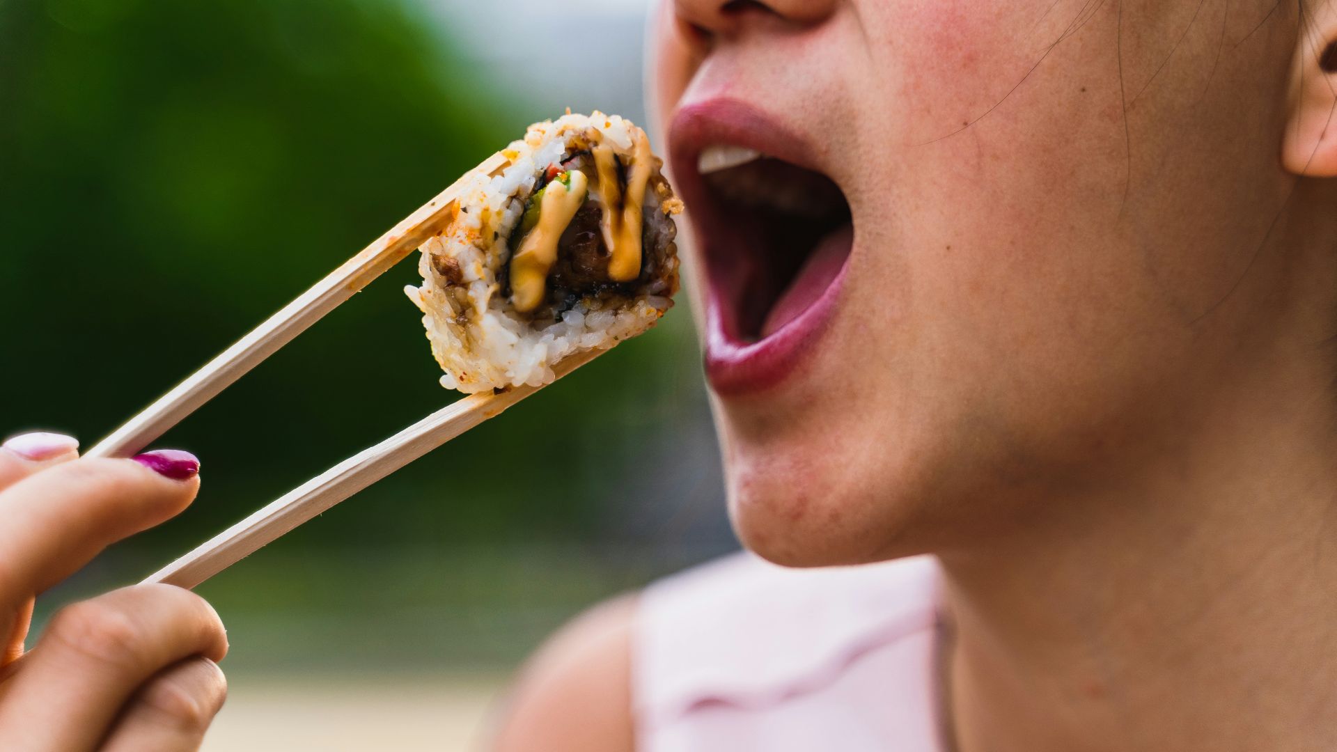 a woman eating a piece of food with chopsticks