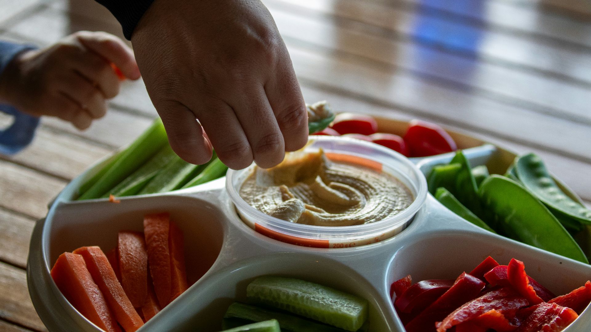 A person dipping dip into a bowl of vegetables