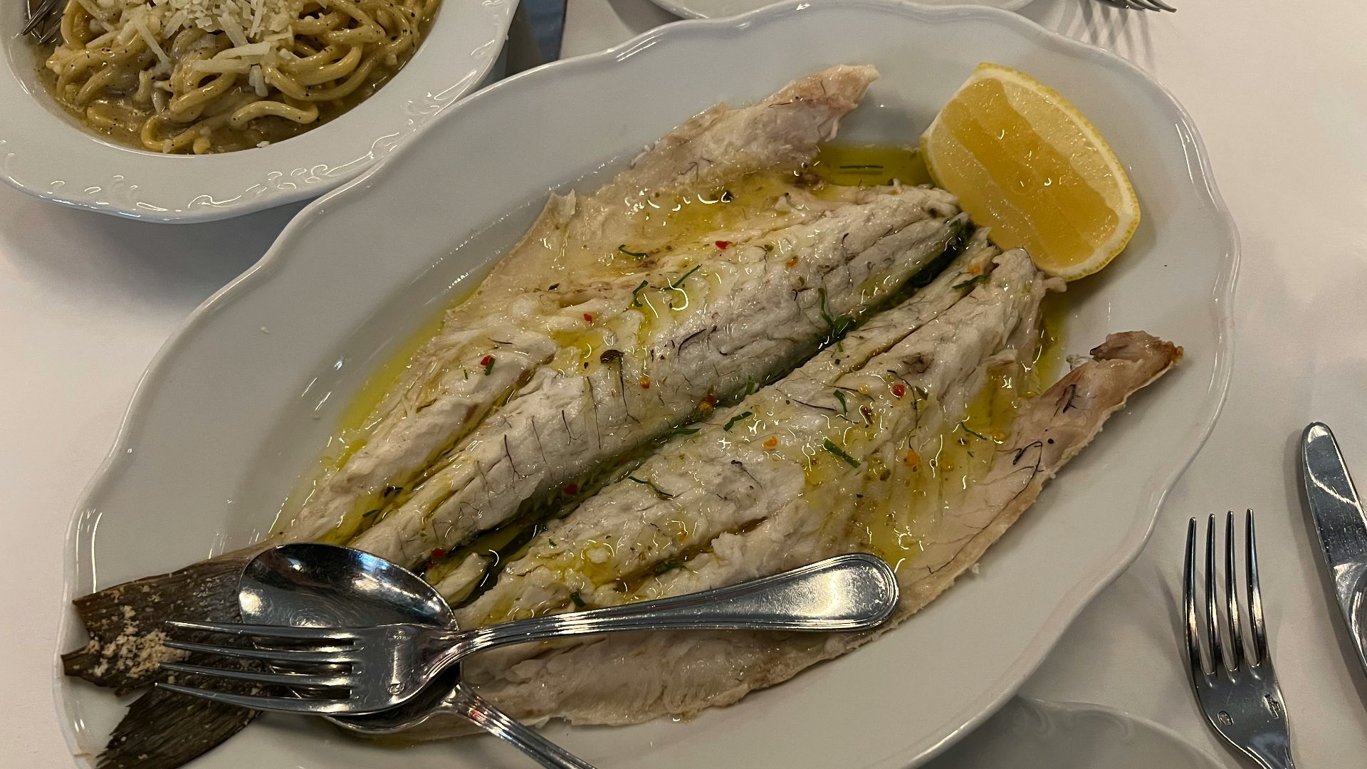 a white plate topped with fish next to a bowl of noodles