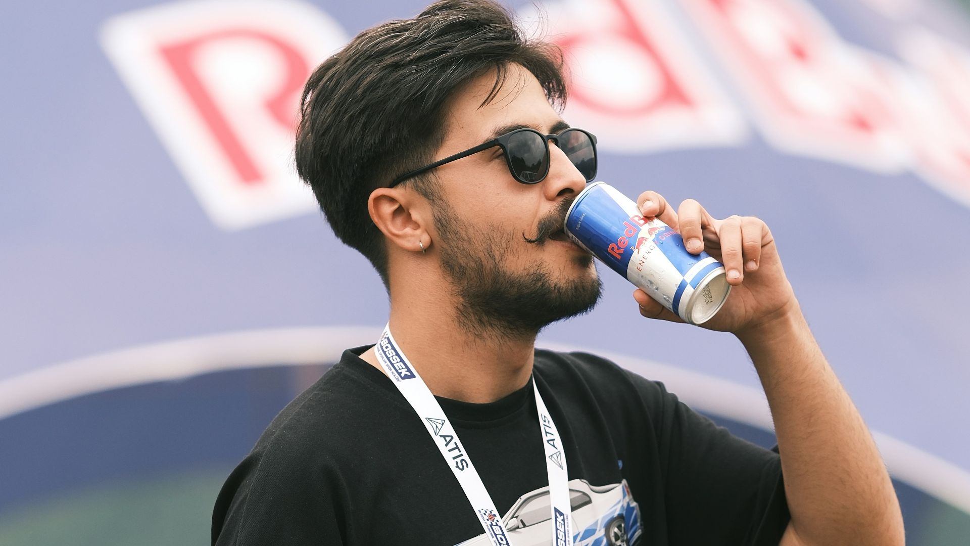 A man drinking from a bottle while standing in front of a red bull tent