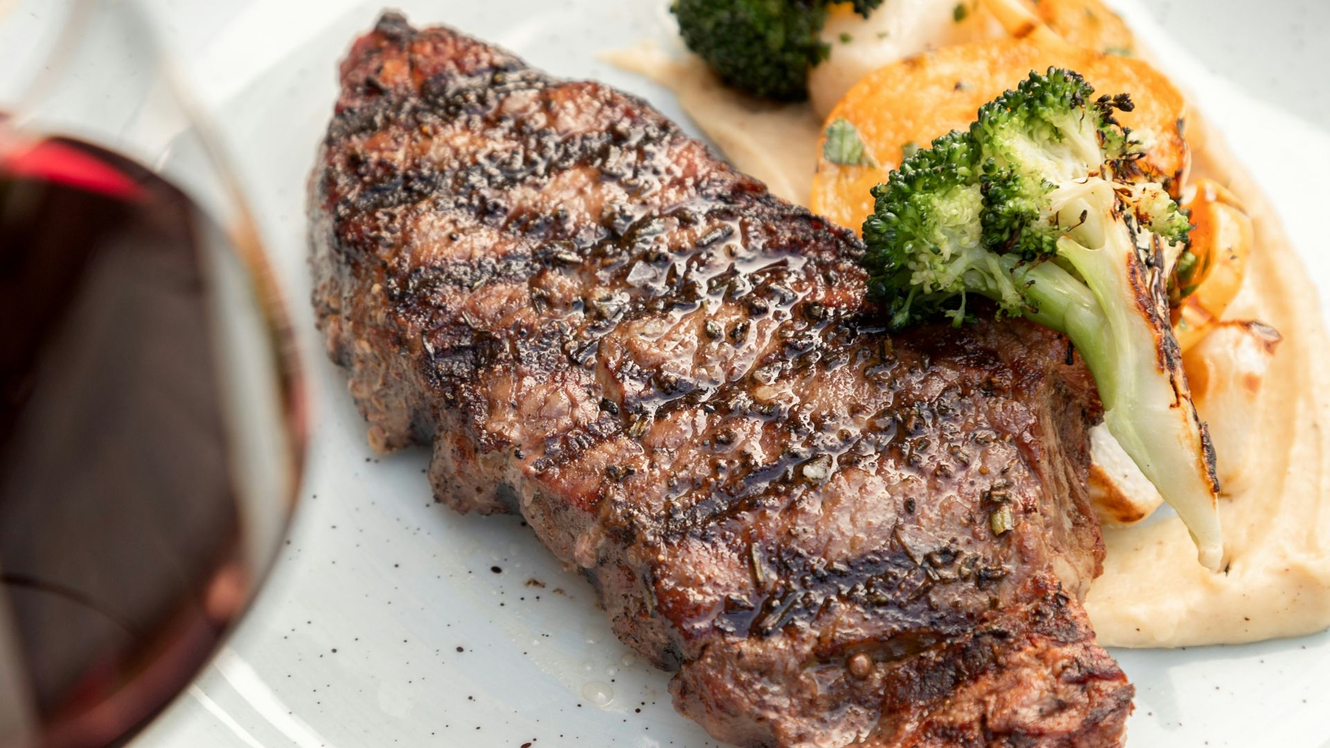 a white plate topped with meat and veggies next to a glass of wine