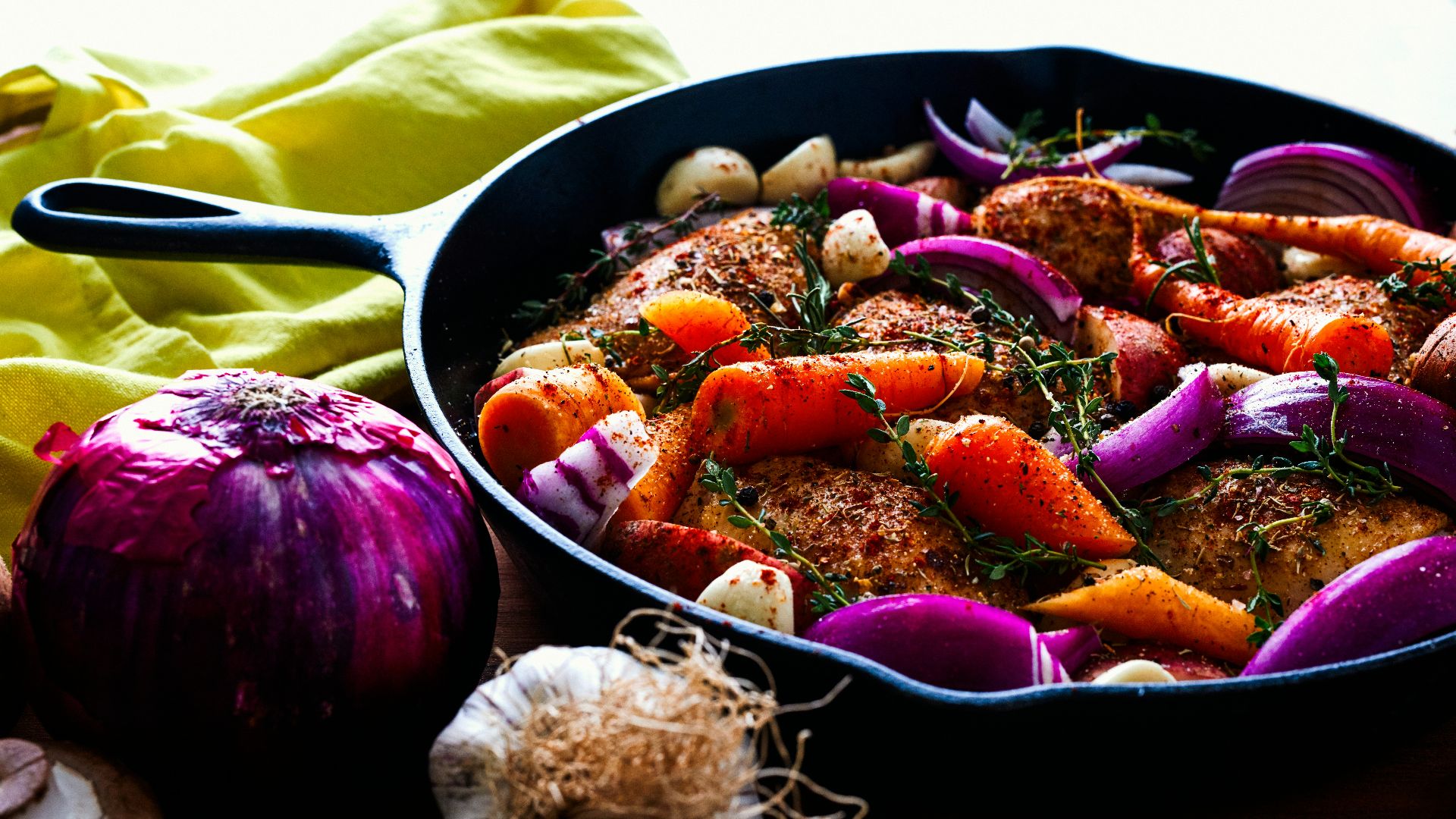 carrots, garlic, onions, and herb spicing meat on skillet