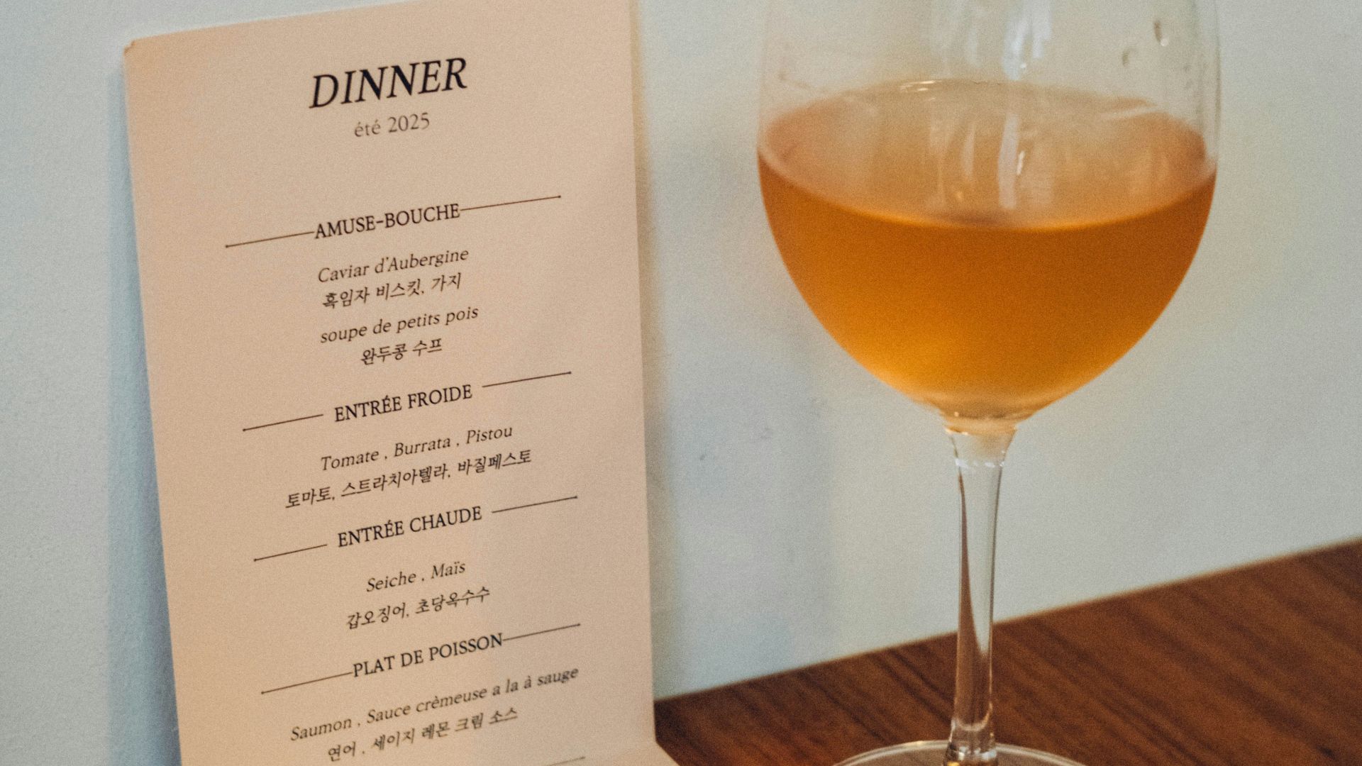 A glass of amber liquid next to a dinner menu.