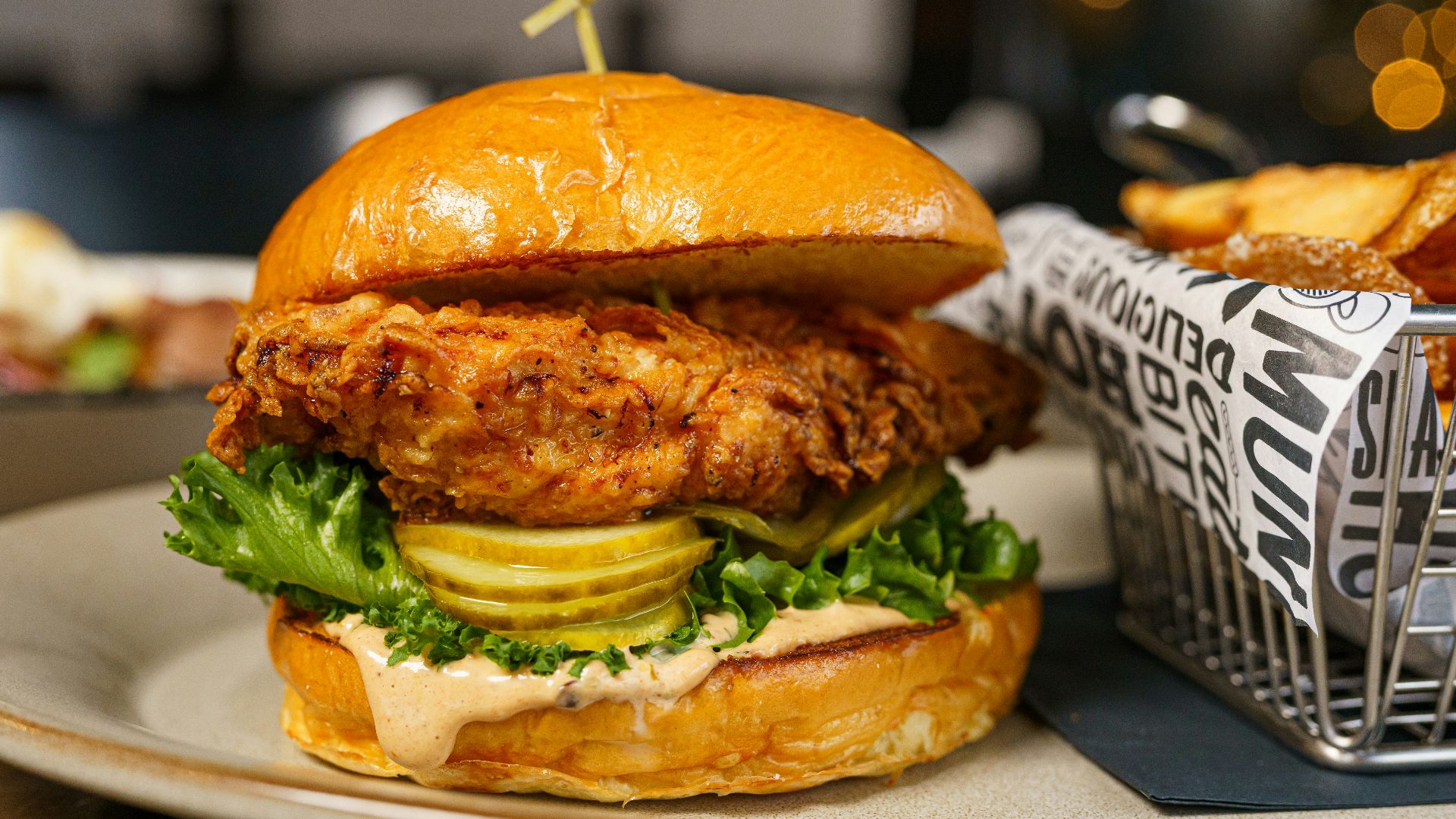 a chicken sandwich on a plate next to a basket of fries