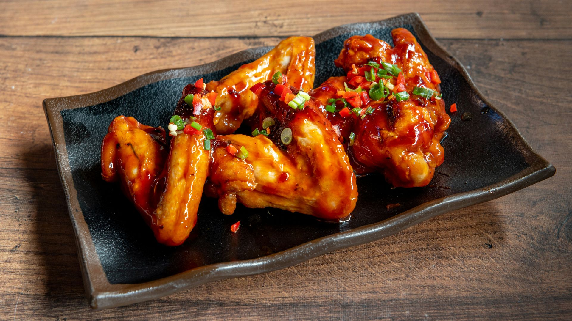 A black plate topped with wings covered in sauce