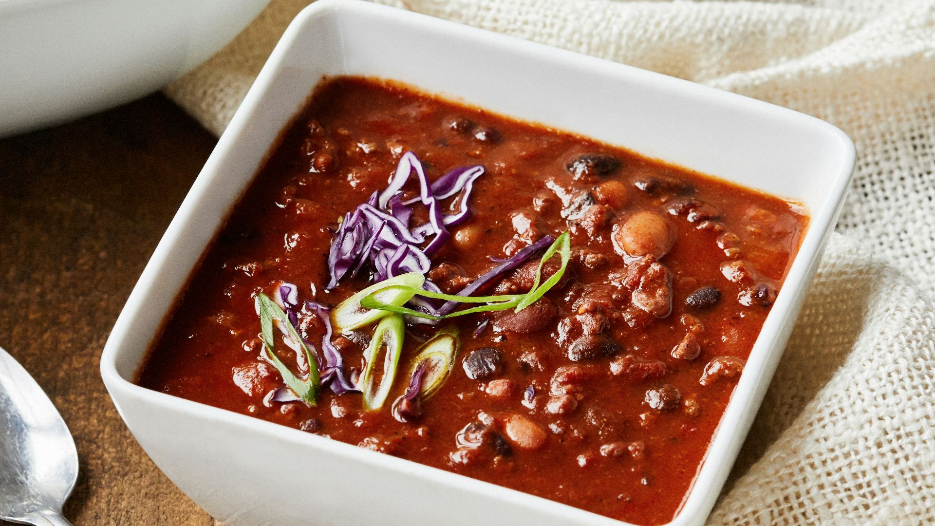 two bowls of chili and a spoon on a wooden table