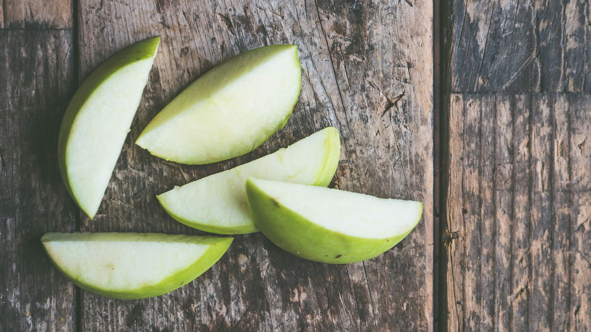 five green apple slices on brown wooden panel