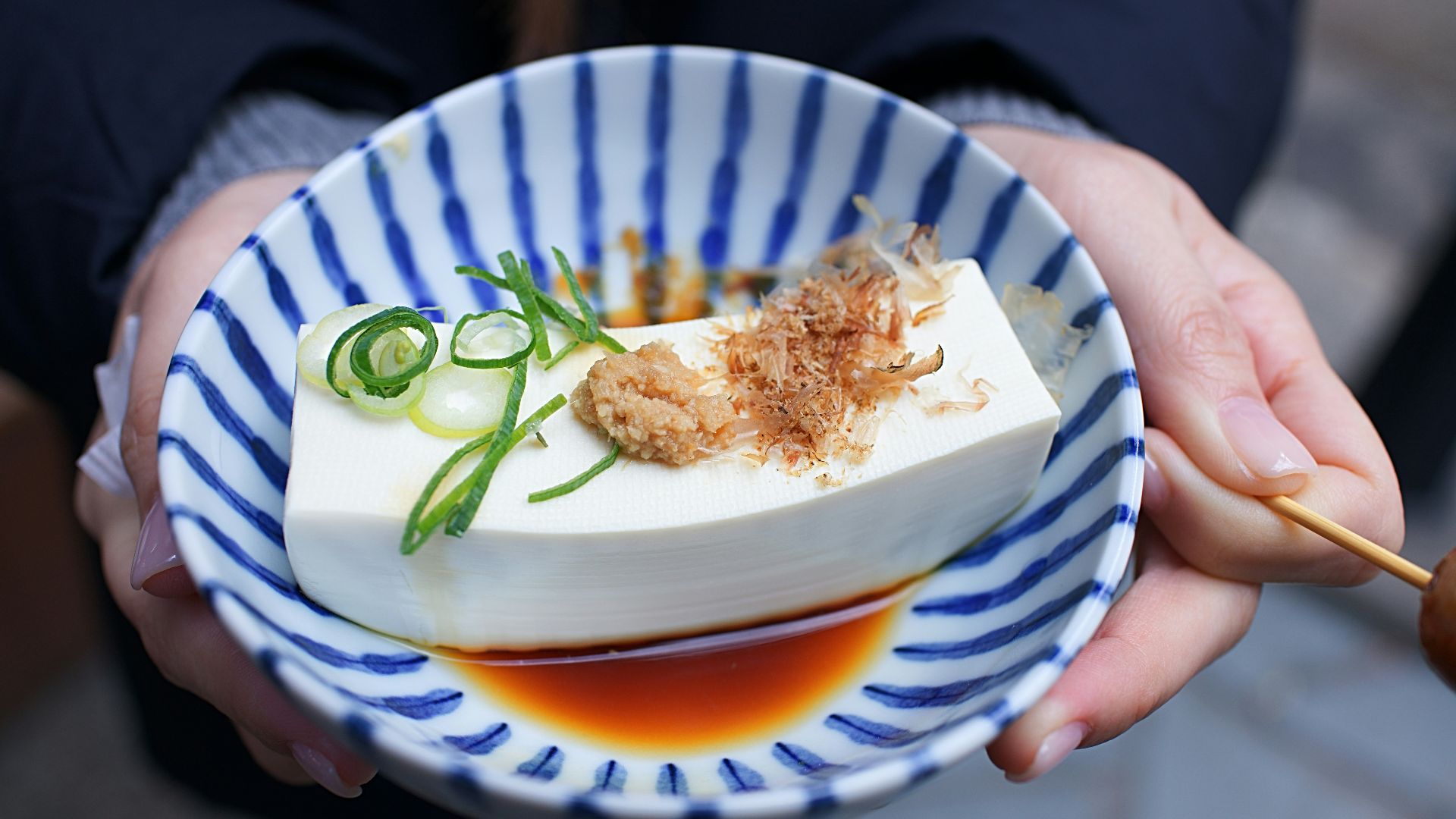 person holding white and blue ceramic plate with rice and sliced cucumber