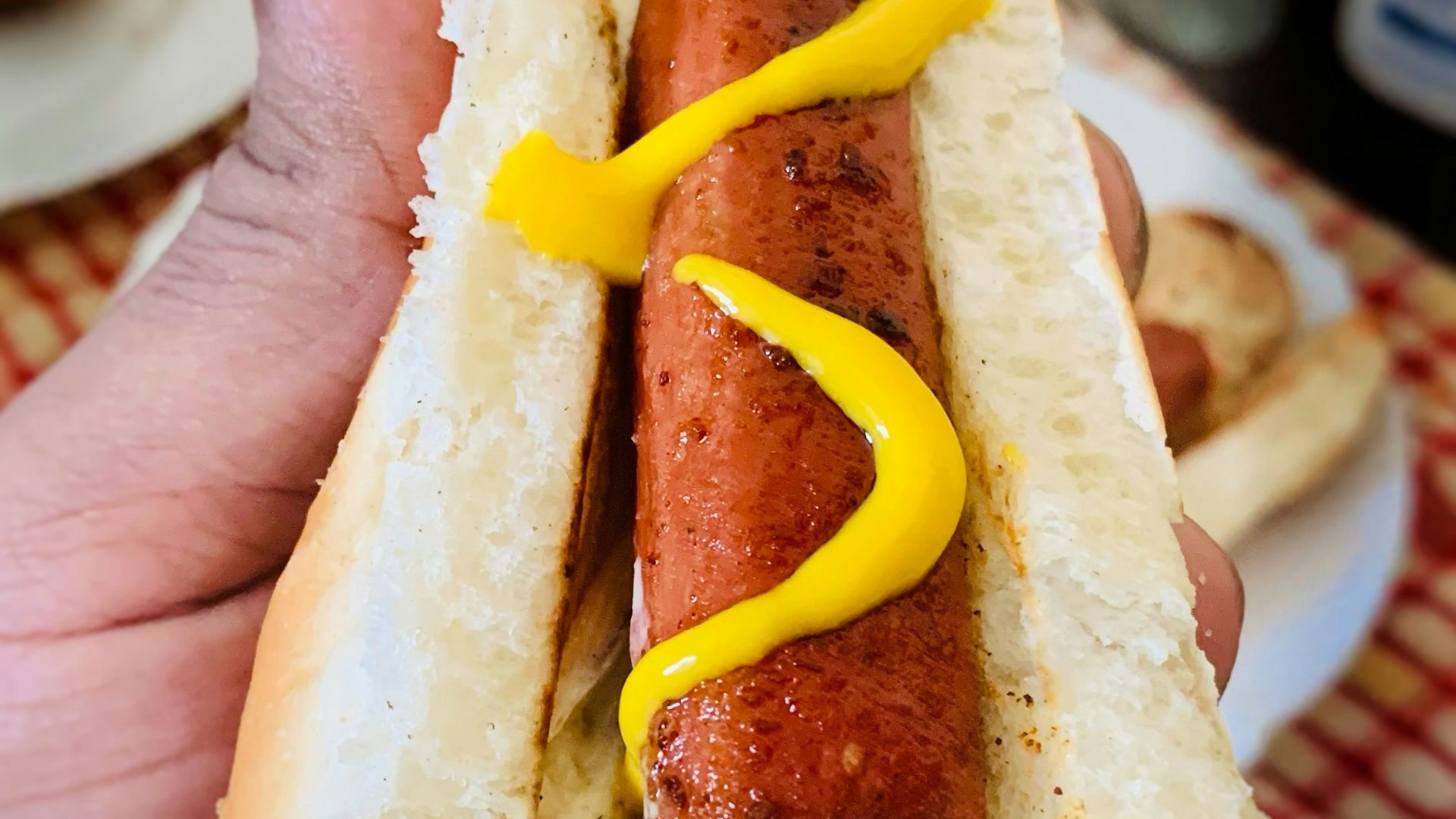 A person holding a hot dog with mustard on it