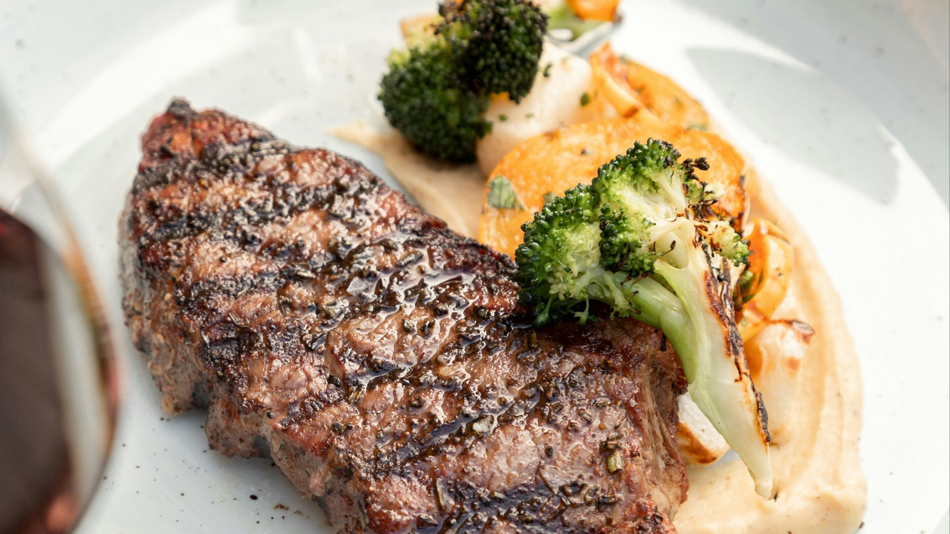 a white plate topped with meat and veggies next to a glass of wine